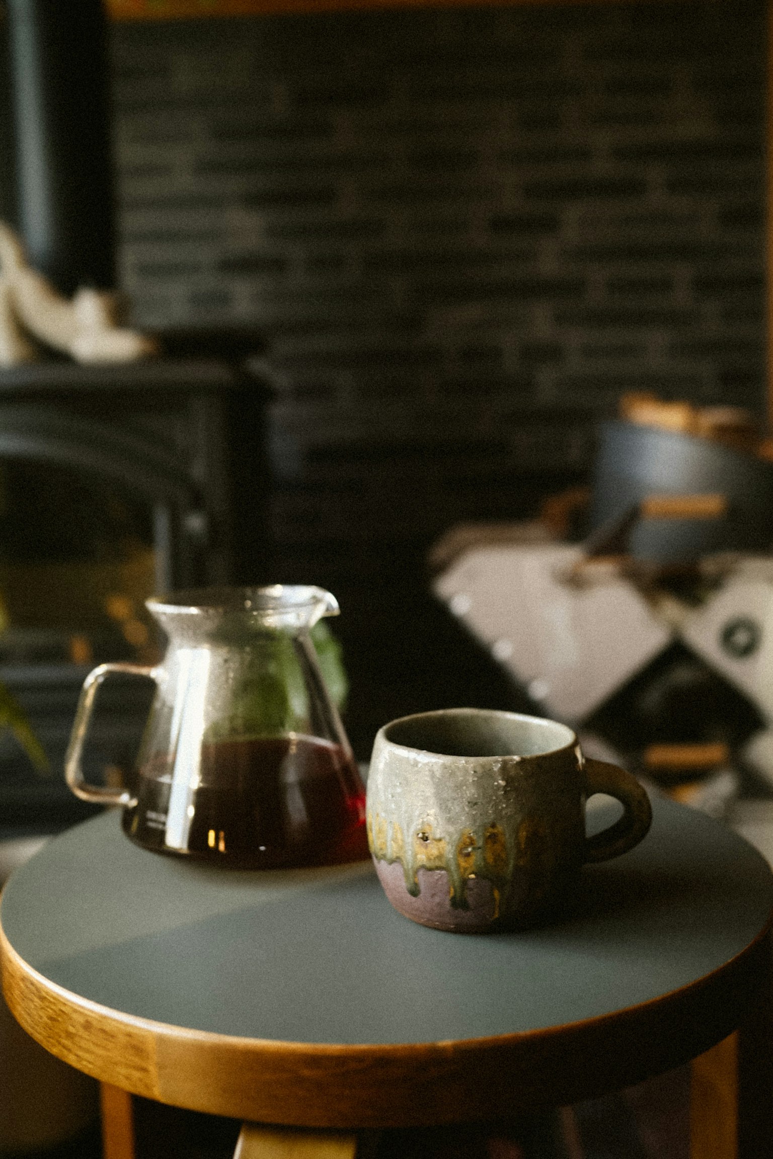 コーヒーを注いだガラスのポットと陶器のマグカップが木製のテーブルに置かれているシーン