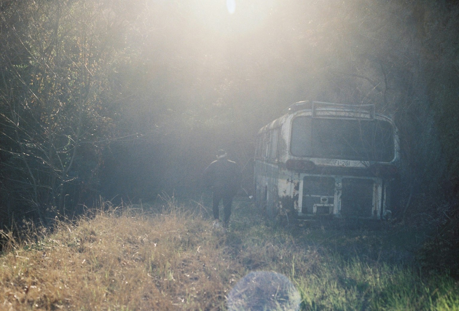 Un vieux bus dans un environnement brumeux avec de l'herbe haute et une personne marchant