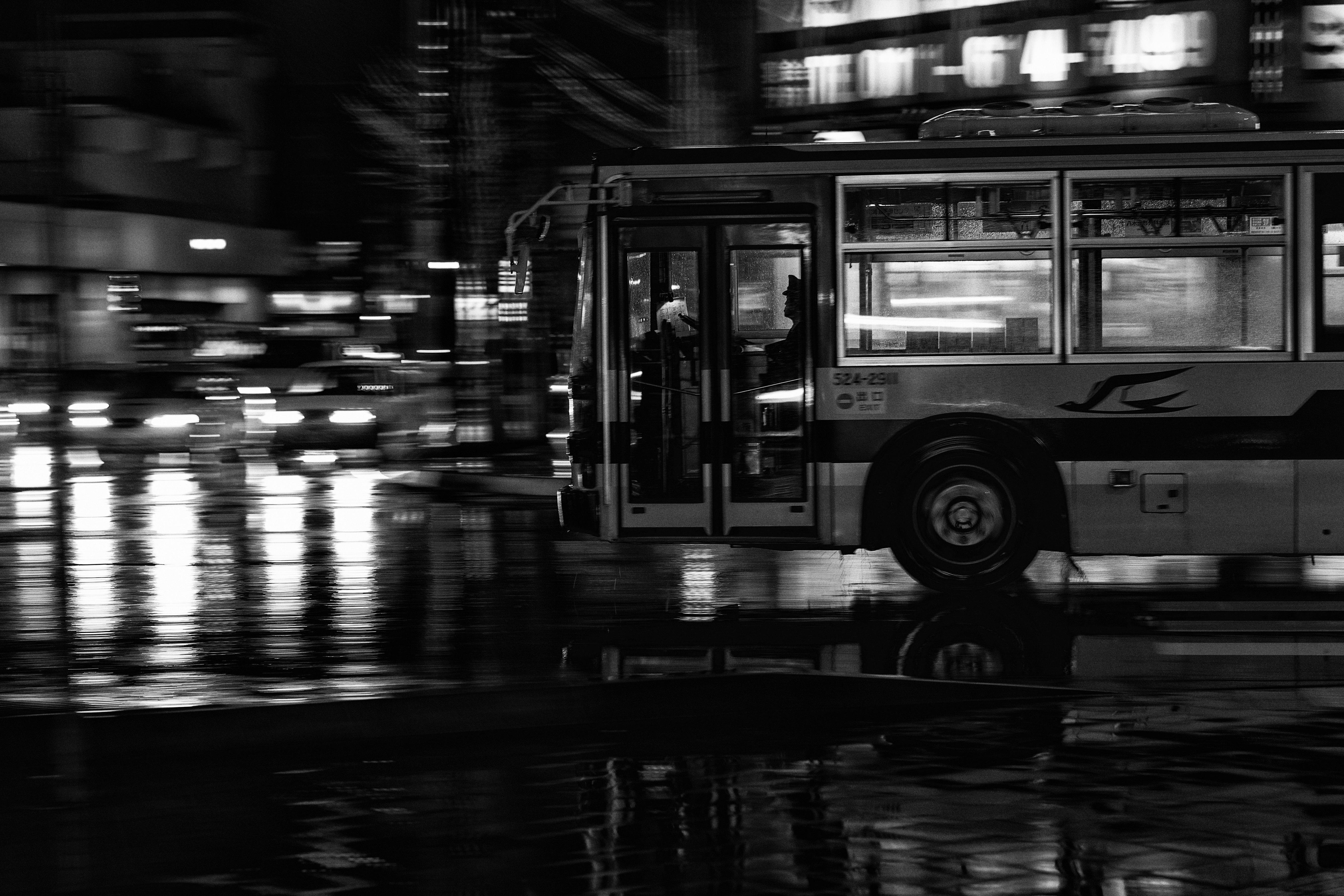 雨上がりの夜、駅前を走るバスと濡れた路面の反射