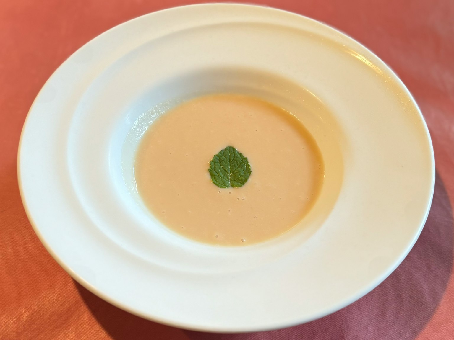 Zuppa cremosa in una ciotola bianca con guarnizione di erbe verdi