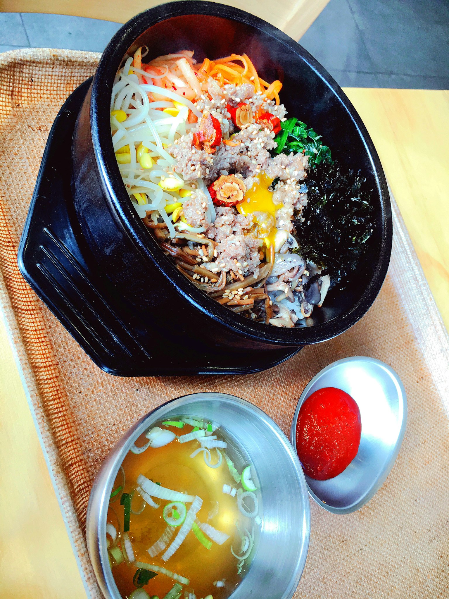 Bibimbap in einer Steinschüssel mit Gemüse und Fleisch serviert mit Suppe