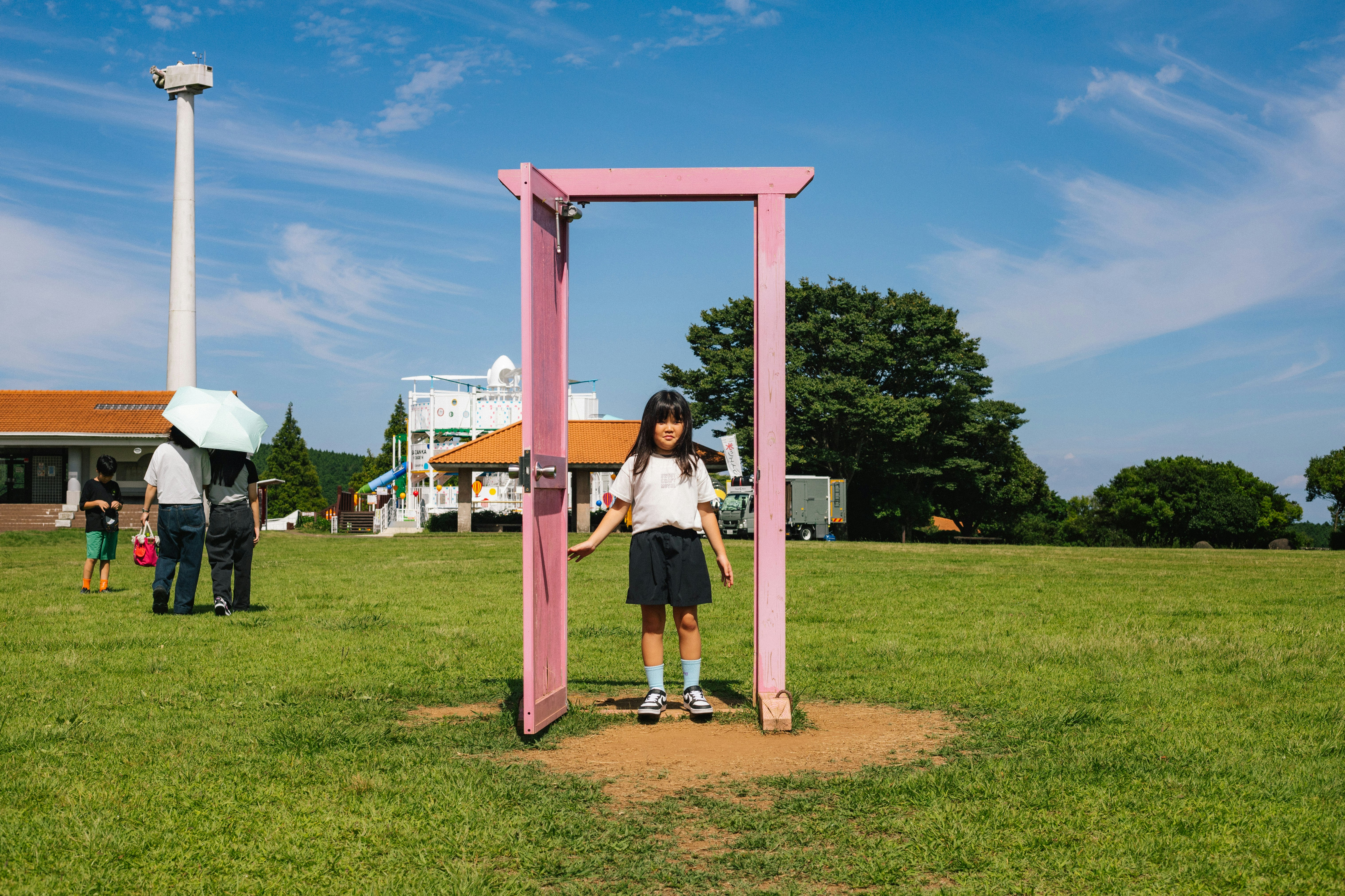 芝生の公園でピンクの門の前に立つ子ども