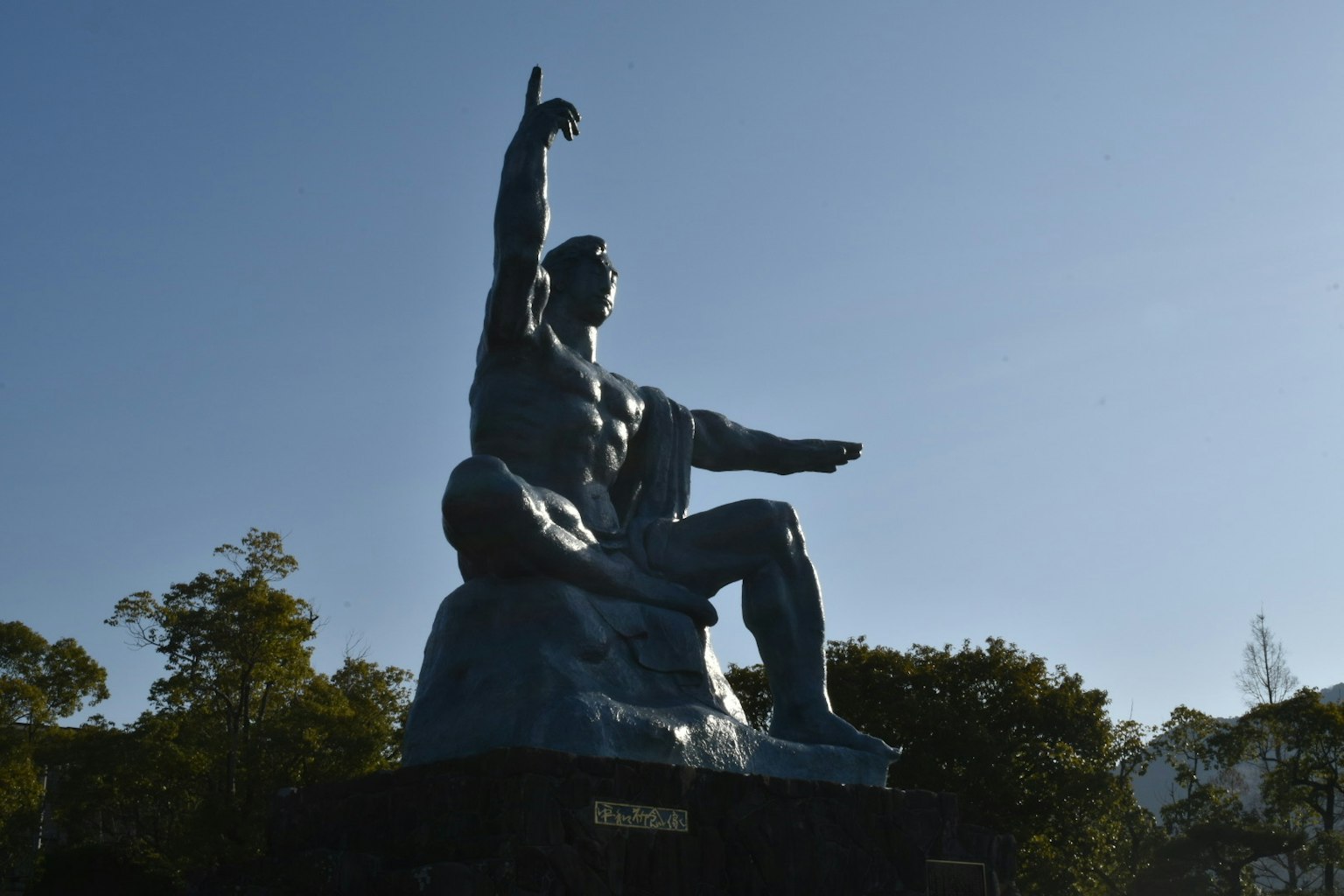 Una escultura poderosa bajo un cielo azul que representa a un hombre con una mano levantada y la otra extendida hacia adelante