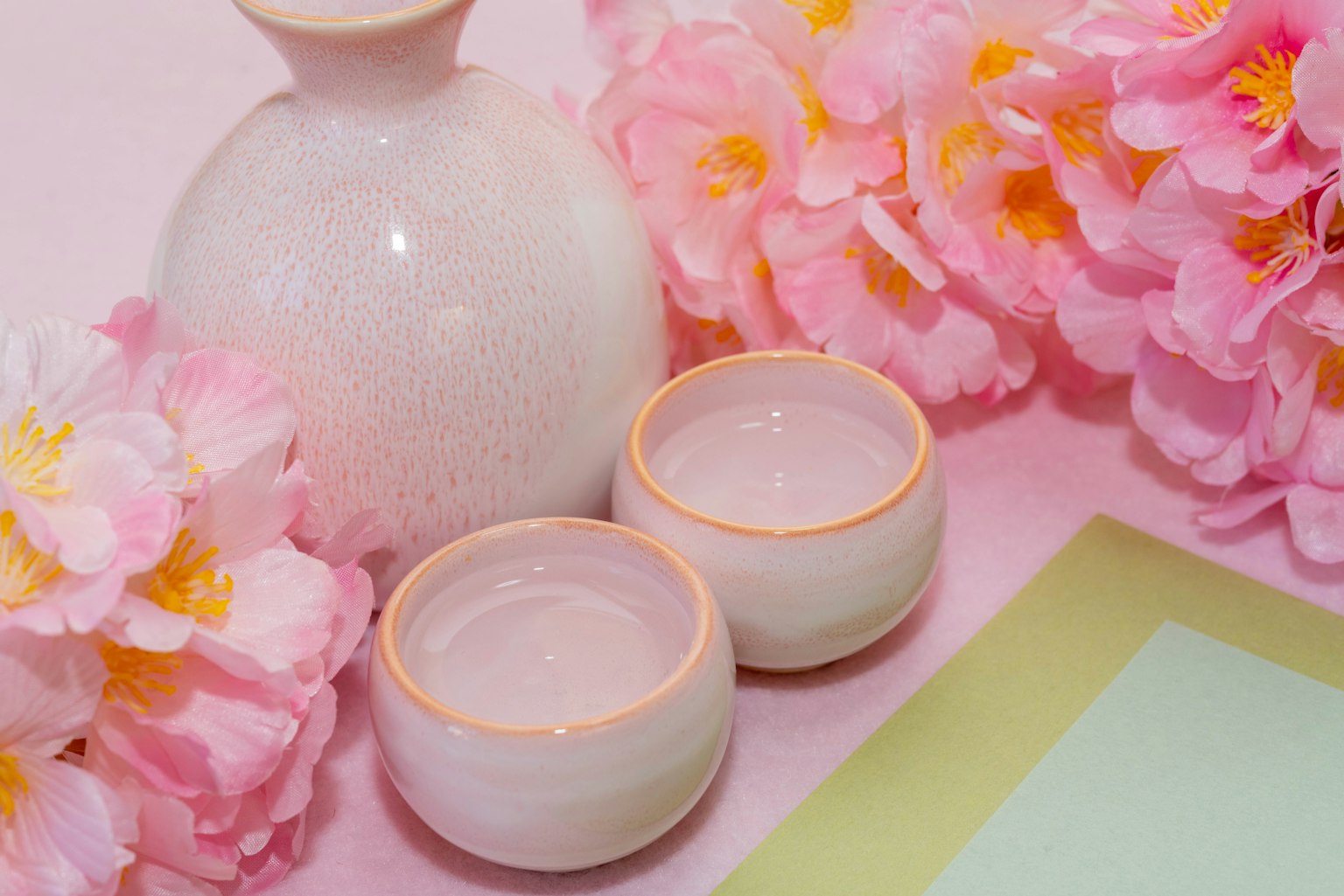 Hoa hồng nhạt với bình sake gốm trắng và hai cốc nhỏ
