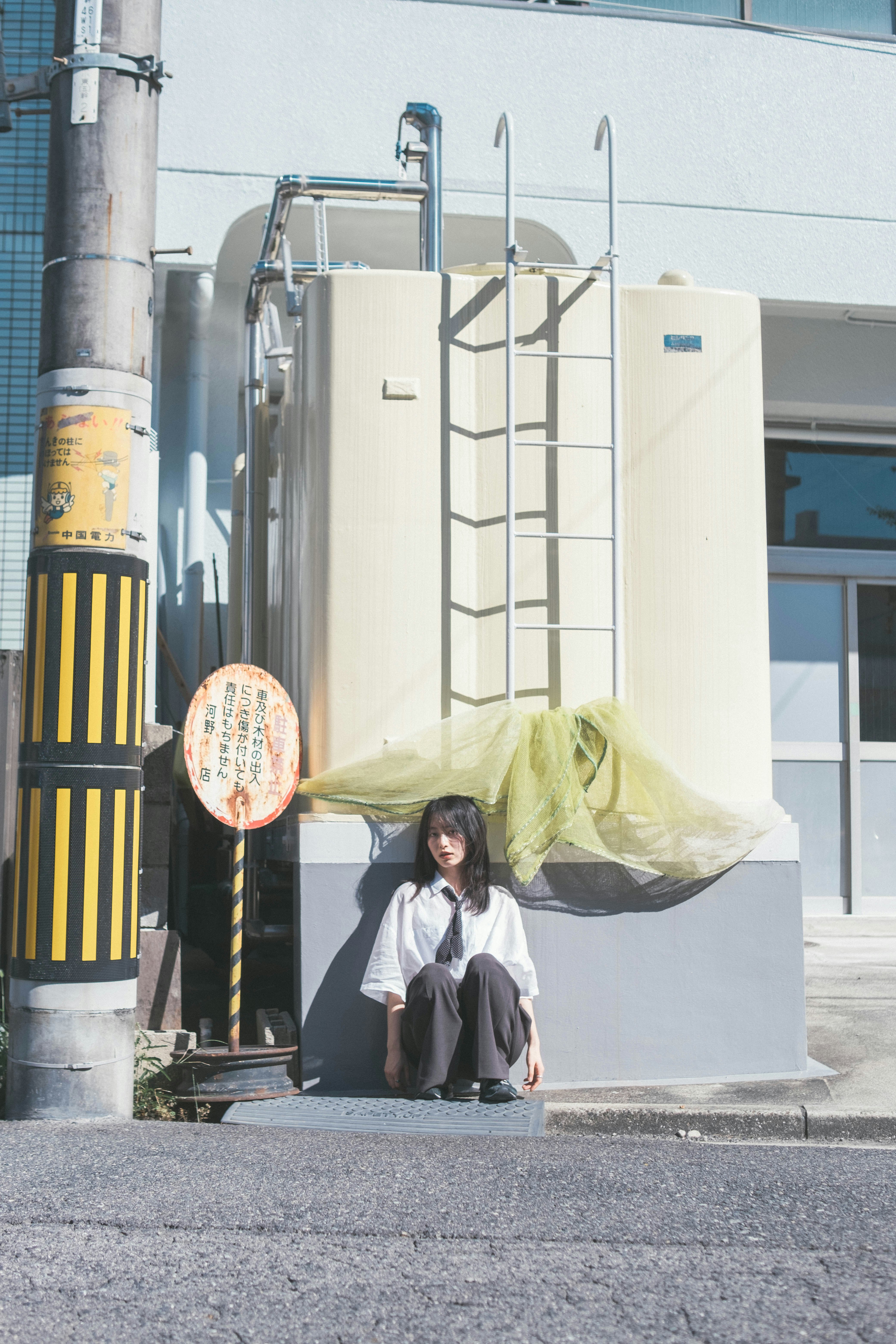 person sitting by industrial facility wall with laddered equipment