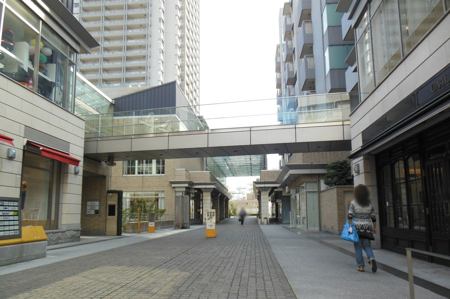 Modern commercial buildings and walkway scene with an overhead bridge structure and people walking