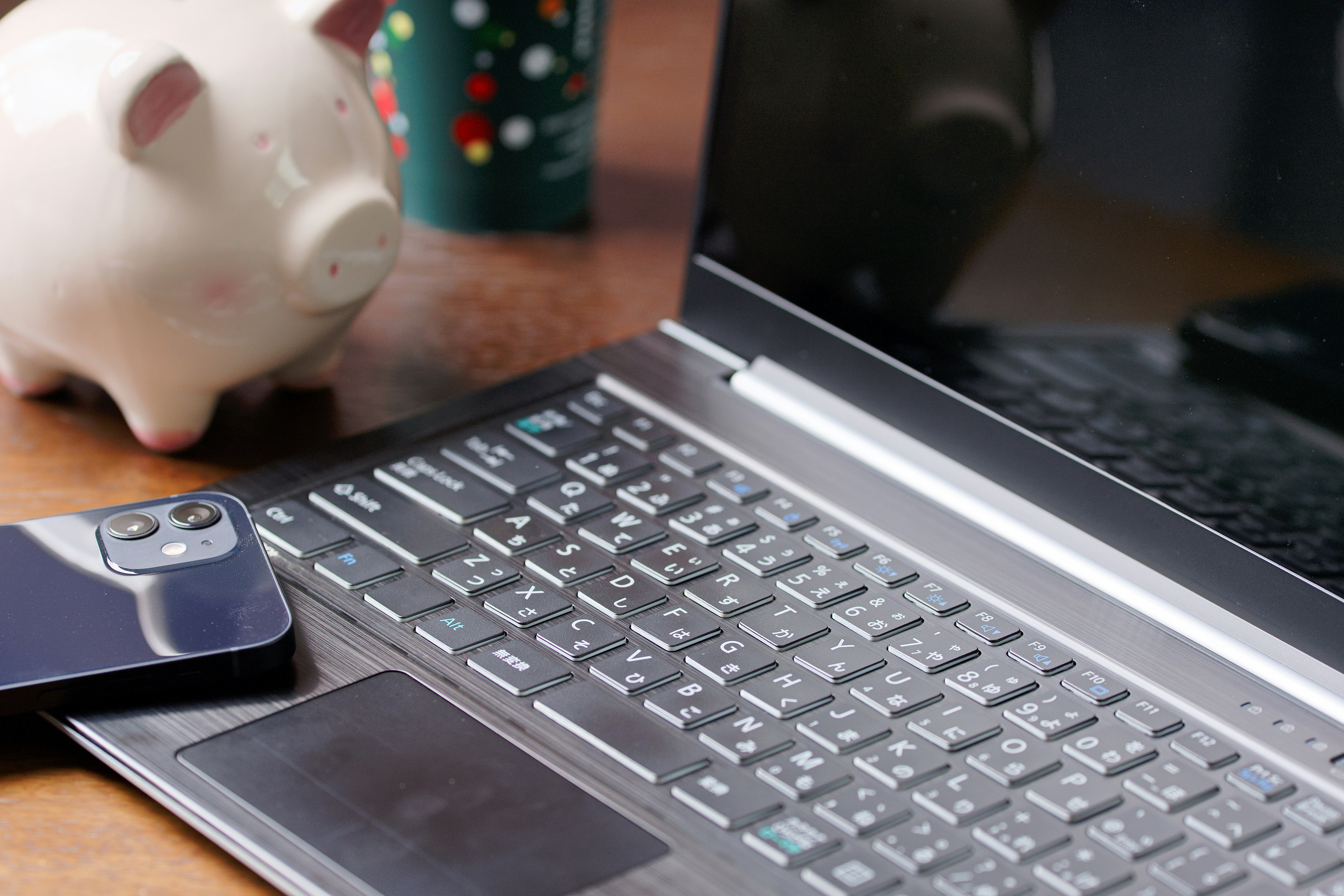 貯金箱とスマホ、ノートPCのあるデスク上の風景