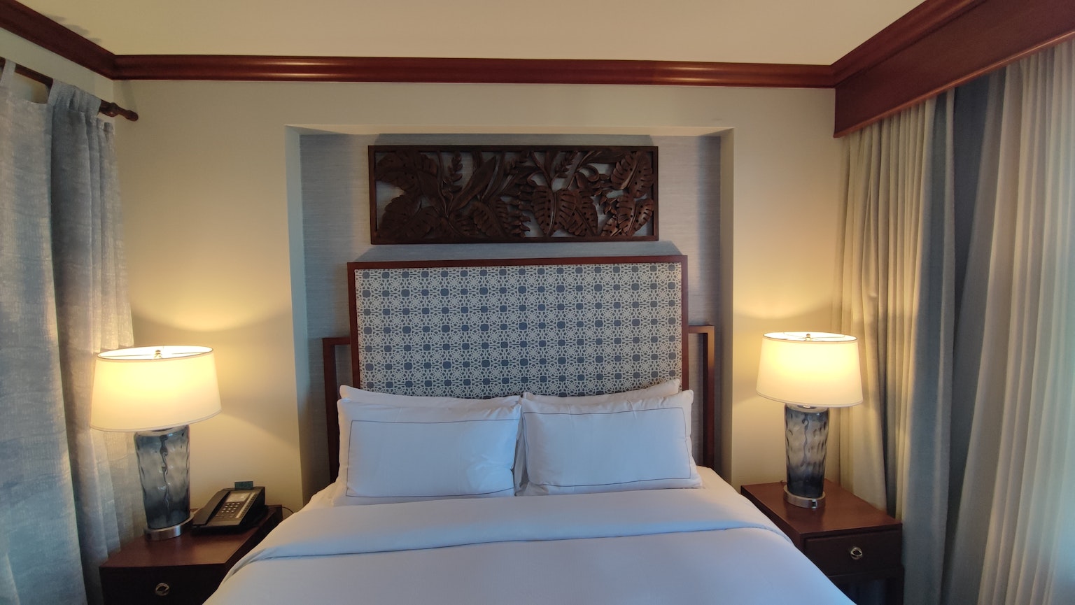 Kamar hotel dengan tempat tidur, kepala tempat tidur dekoratif, lampu, dan tirai