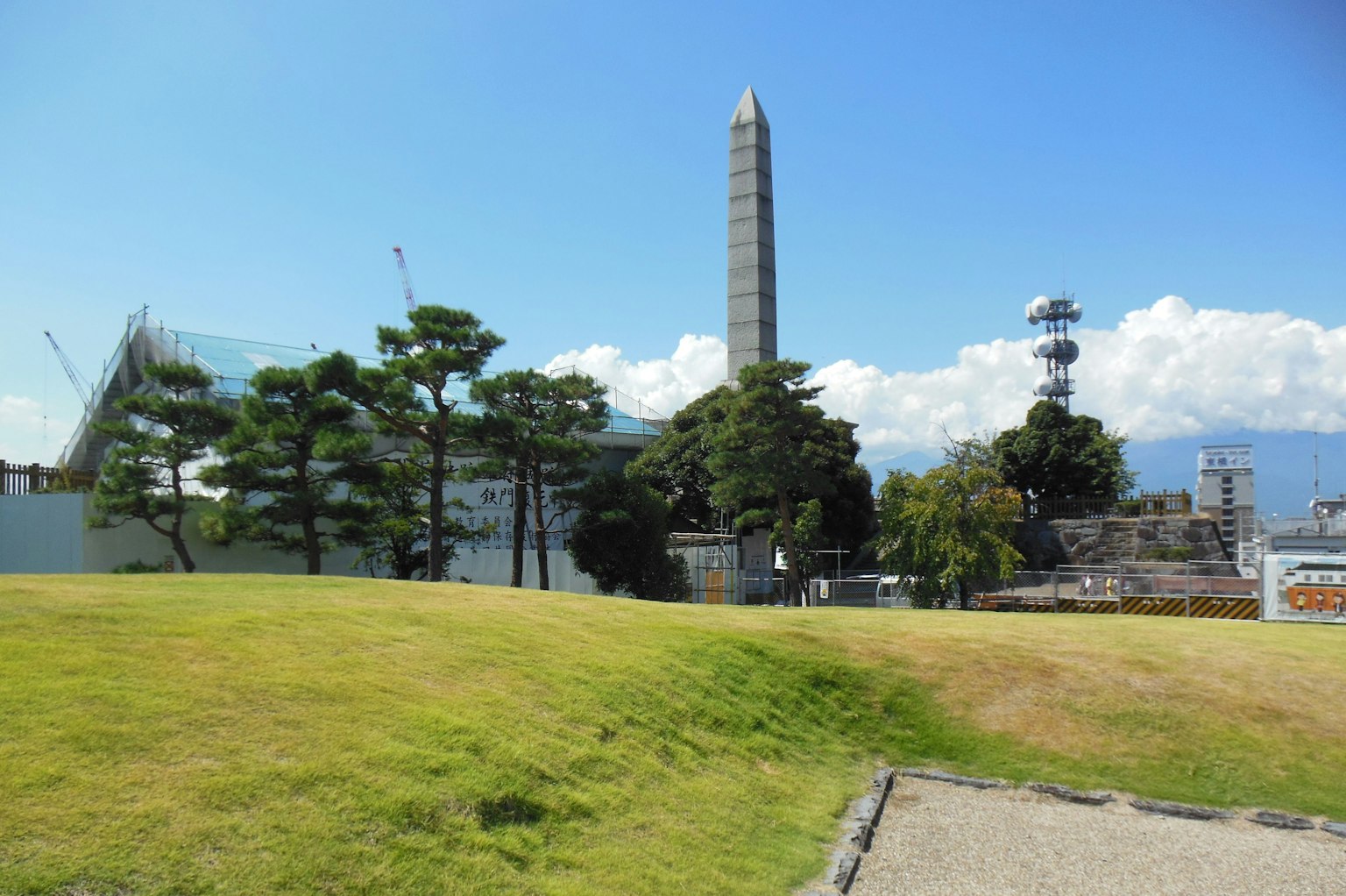 Lanskap dengan rumput hijau dan obelisk menjulang di latar belakang
