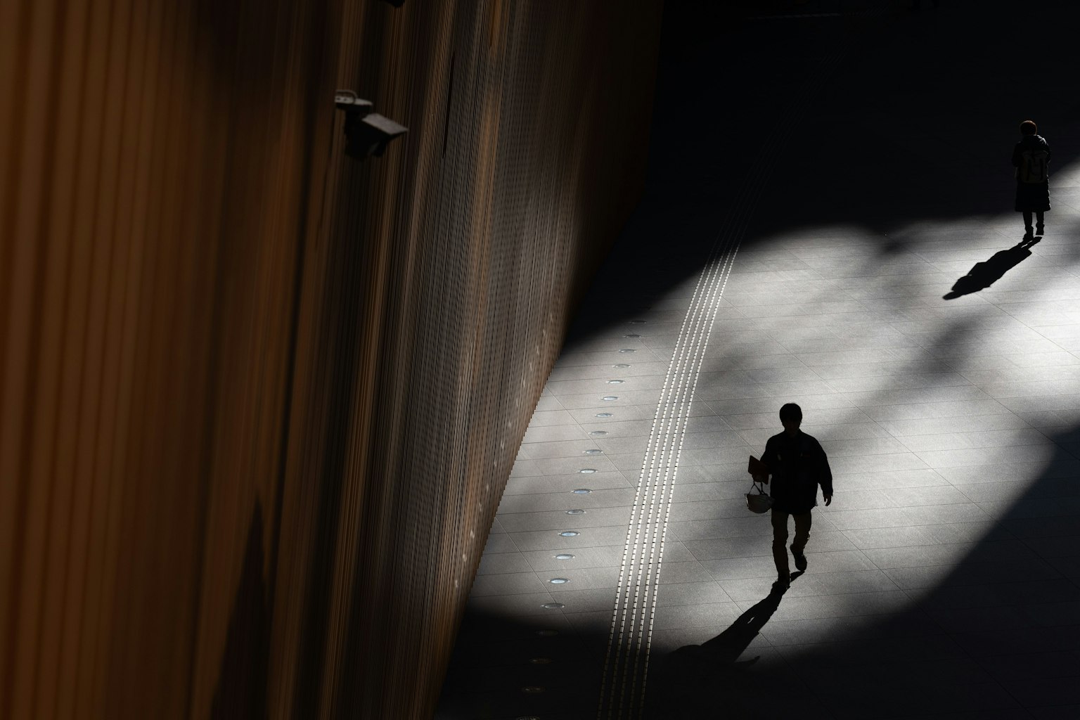 Siluetas de personas caminando en un juego de luz y sombra contrastante en un entorno urbano