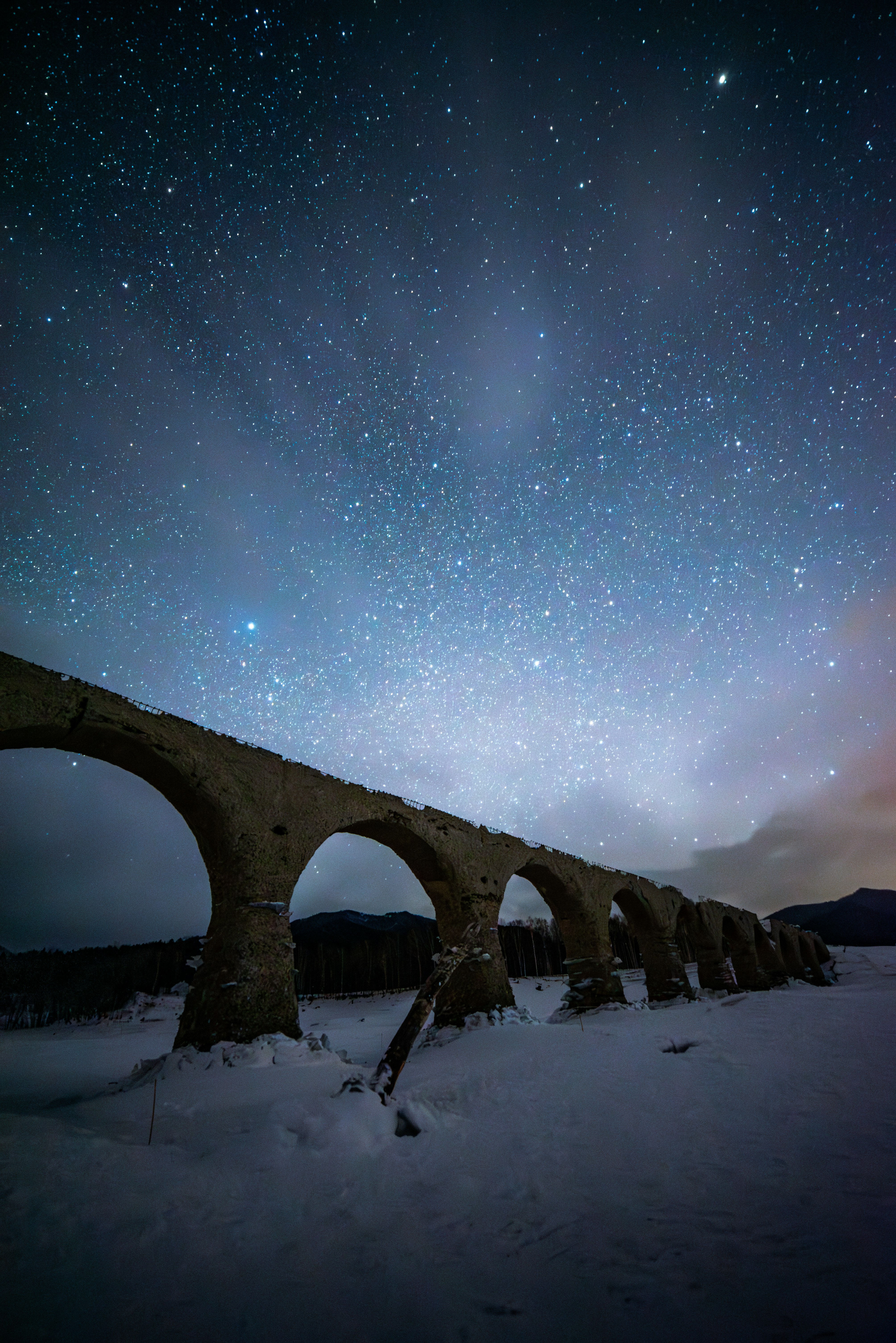 雪原に並ぶ石造りのアーチ橋と満天の星空
