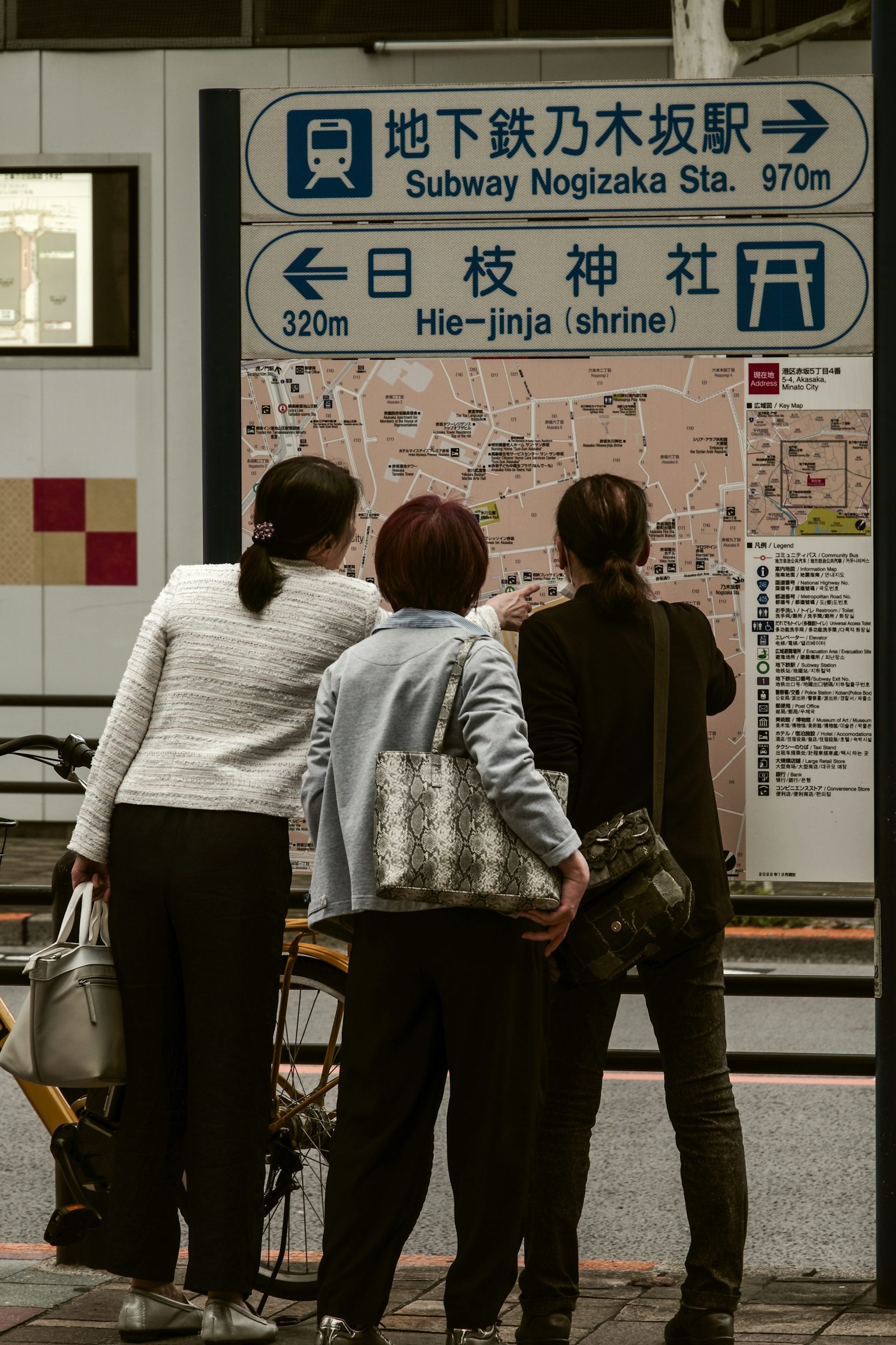 Tres mujeres mirando un mapa en una estación de metro con señales direccionales para la estación Nogizaka y el santuario Meiji