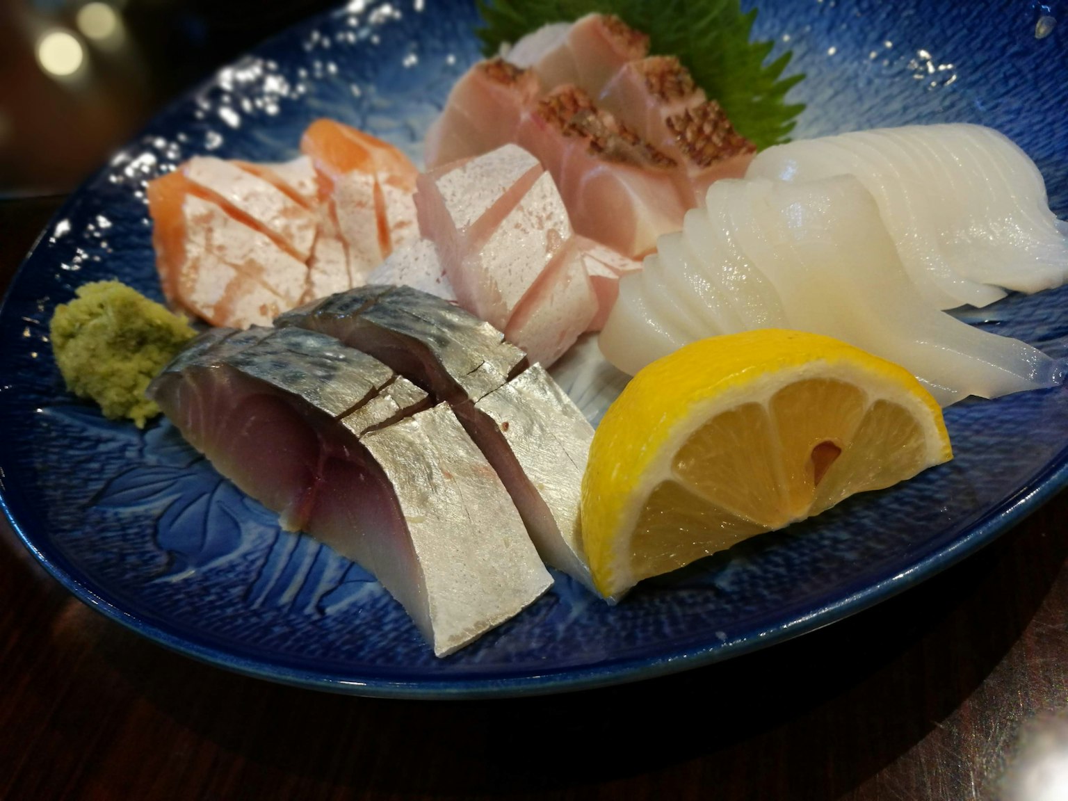 Paduan sushi dan sashimi segar yang berwarna-warni di atas piring biru