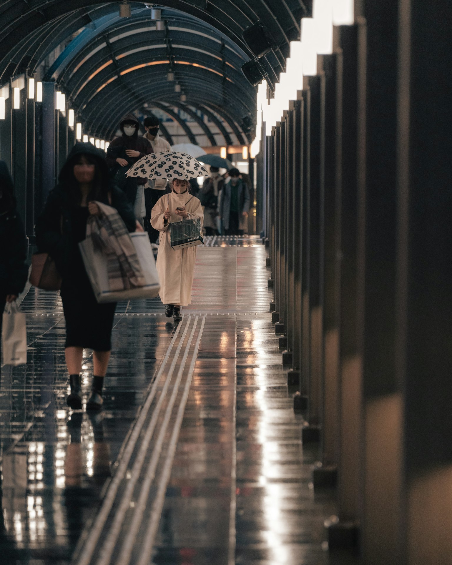 People walking with umbrellas in a glossy corridor