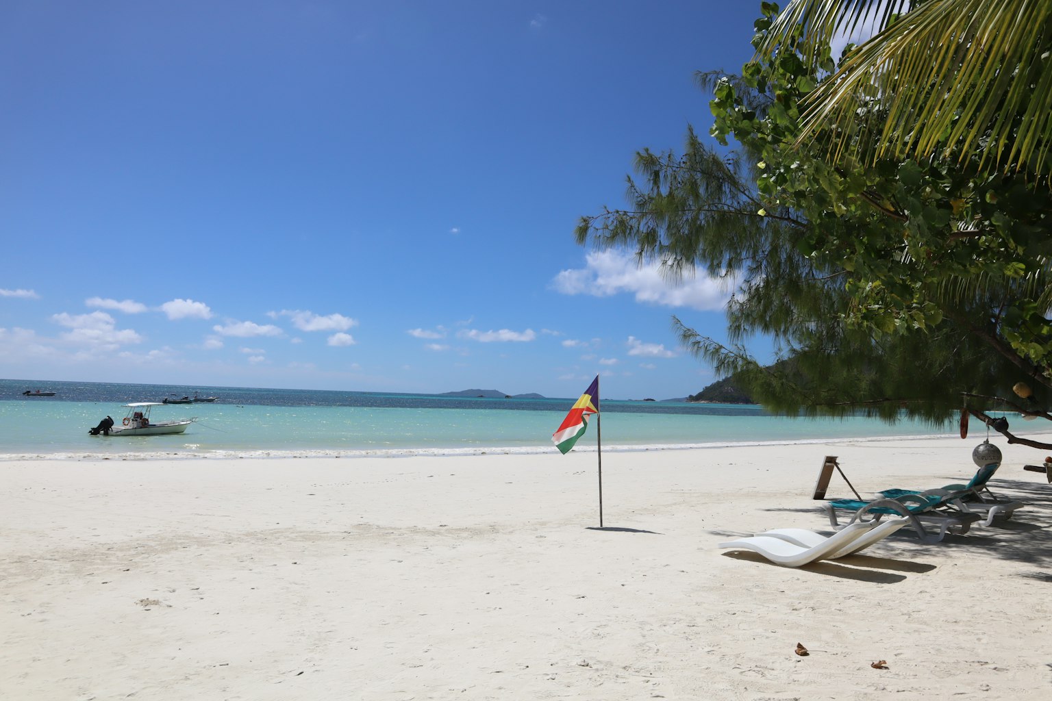 A beach with white sand and clear blue water featuring a colorful flag