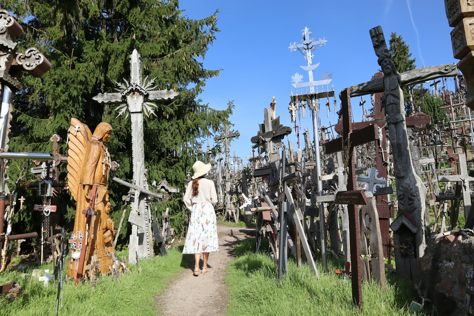 Una donna che cammina lungo un sentiero circondato da croci e sculture Erba verde e cielo blu