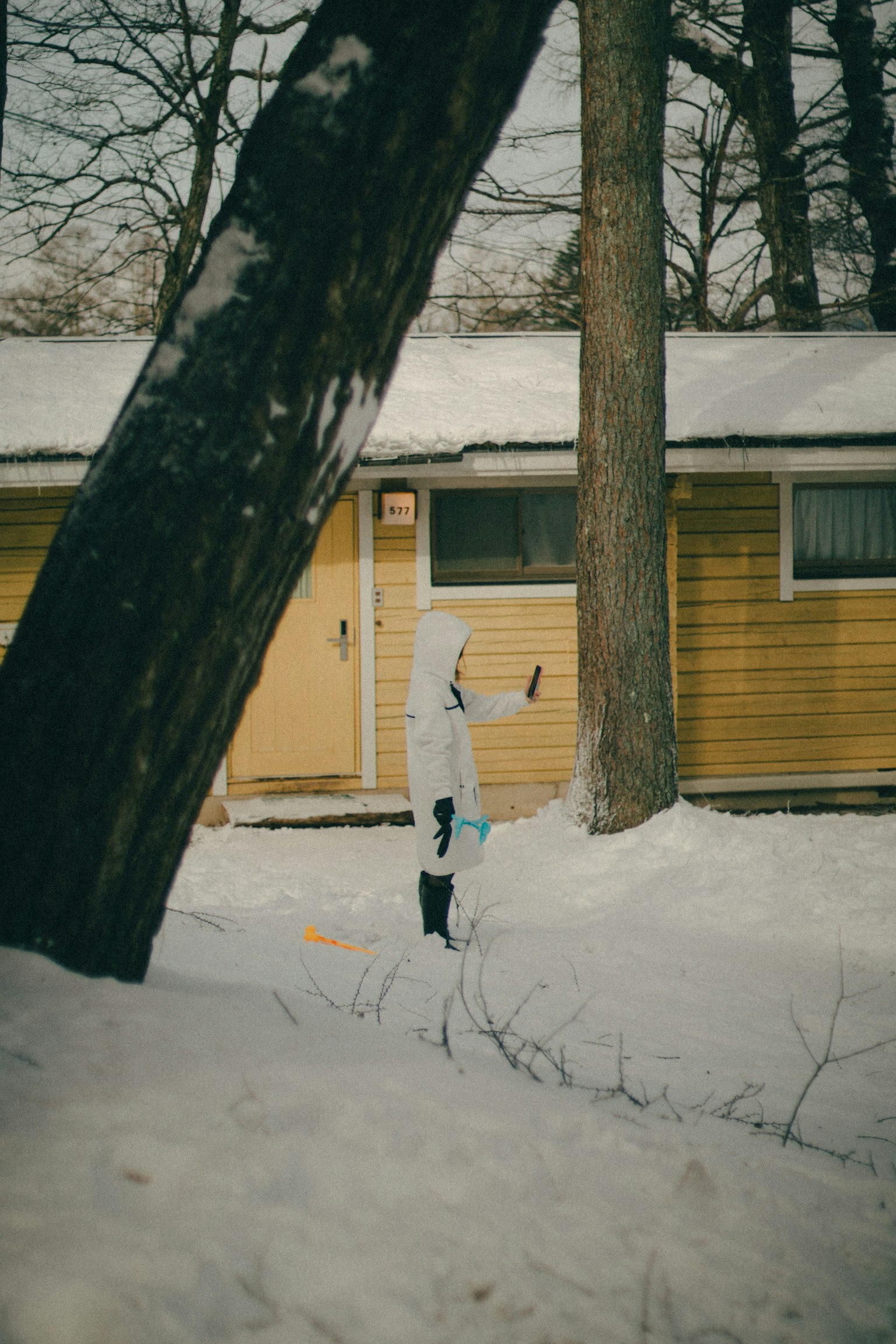 穿白色衣服的孩子站在雪中，背景是黃色小屋