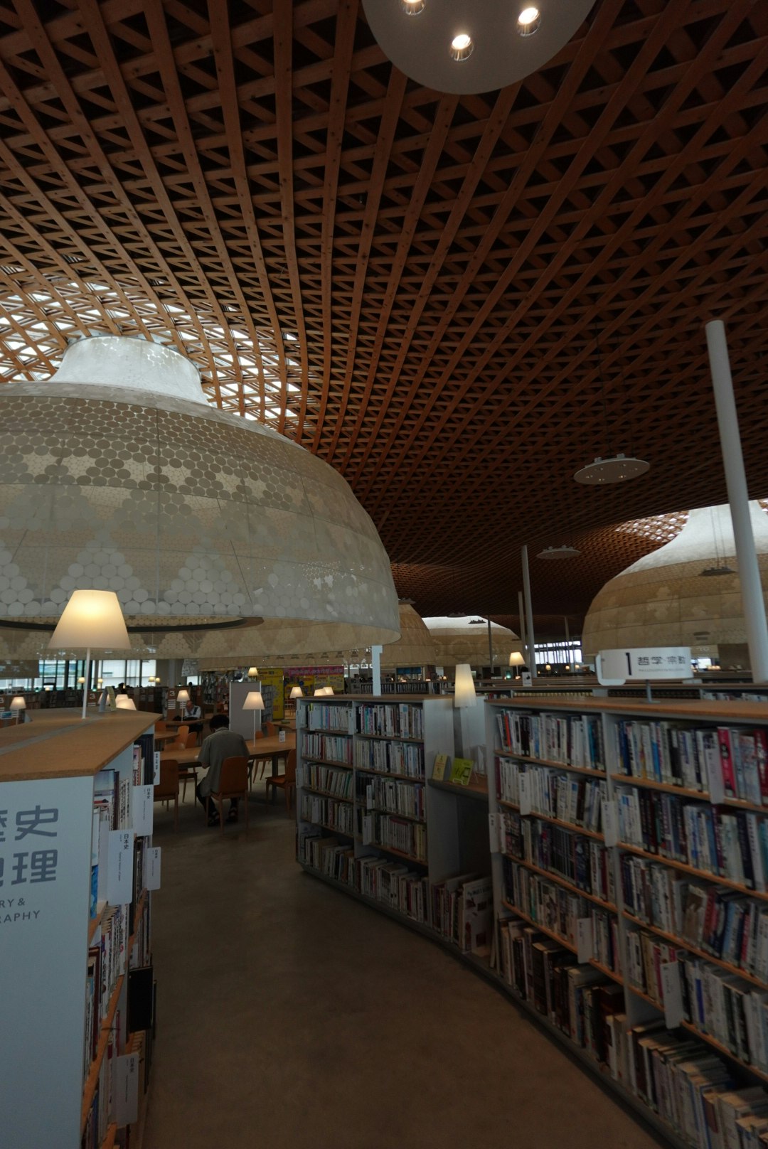 Lorong perpustakaan indoor berbentuk kubah dengan deretan rak buku dan lampu hangat