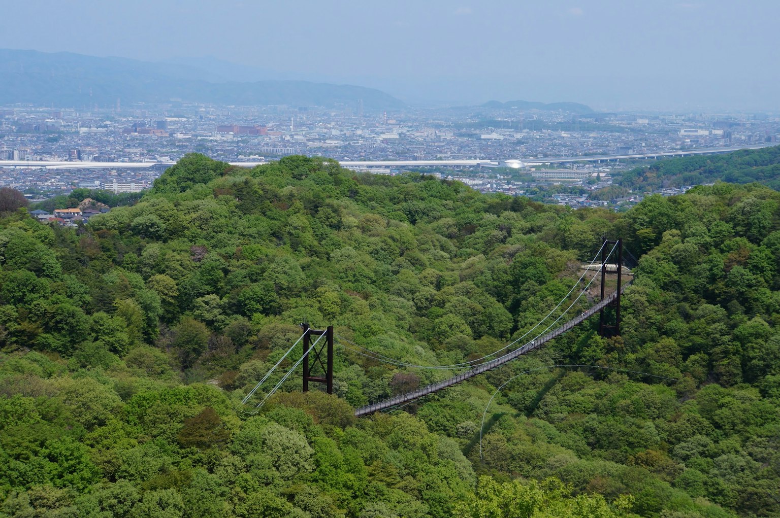 Puente colgante con colinas verdes y paisaje urbano de fondo