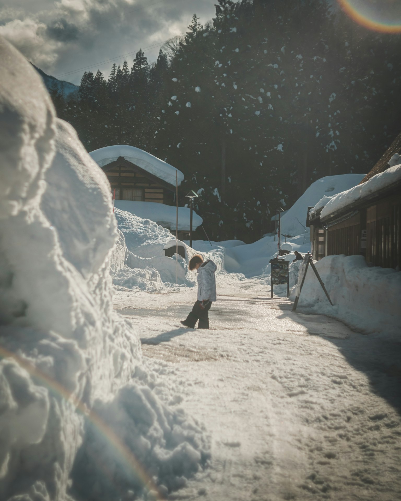 Personne marchant sur un chemin enneigé dans un village avec des tas de neige