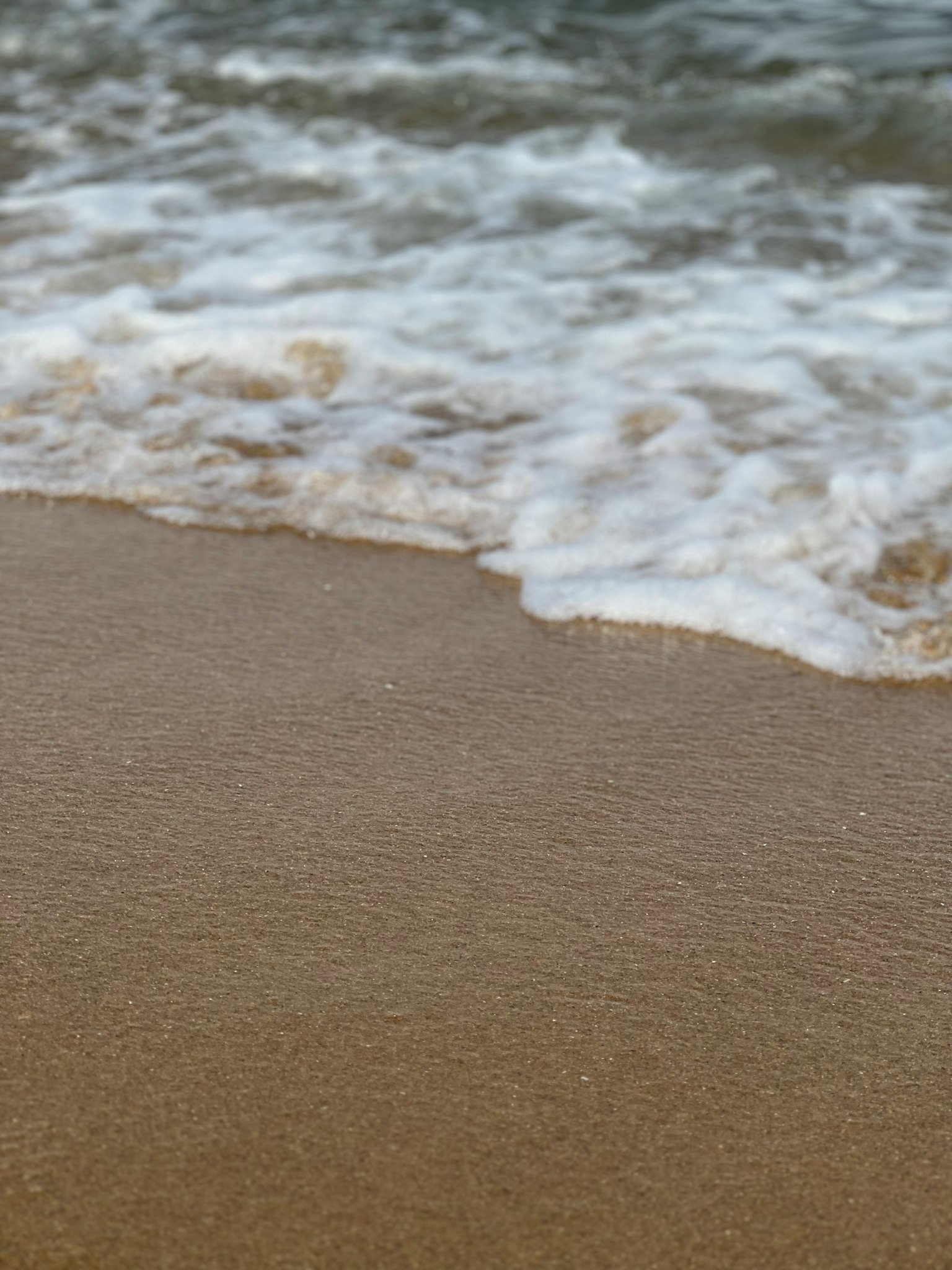 การซูมเข้าไปที่คลื่นเบา ๆ ที่ซัดเข้าหาชายหาดทราย