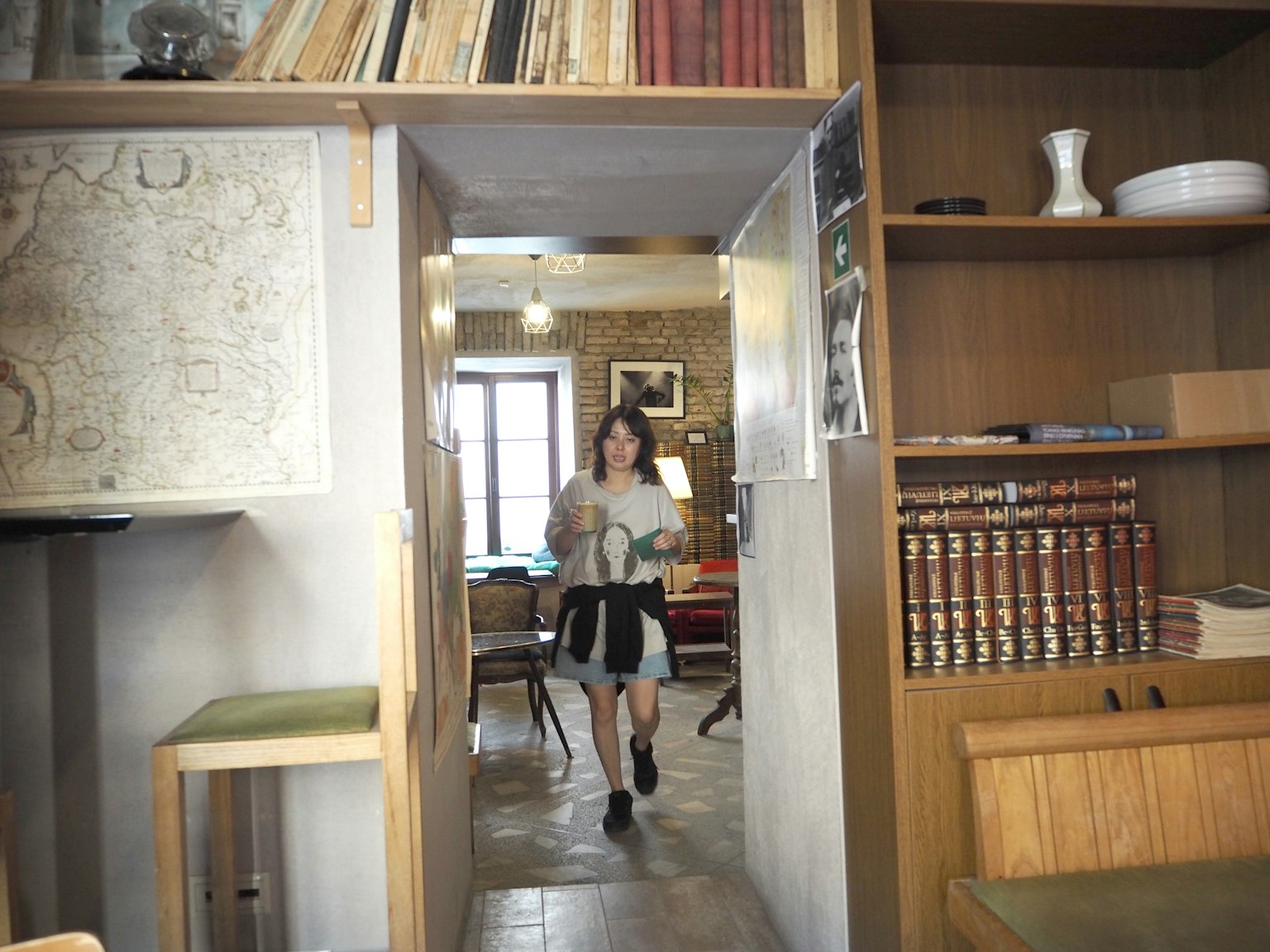 一名女性走進一個溫馨的咖啡館，裡面有木製書架和溫暖的氛圍