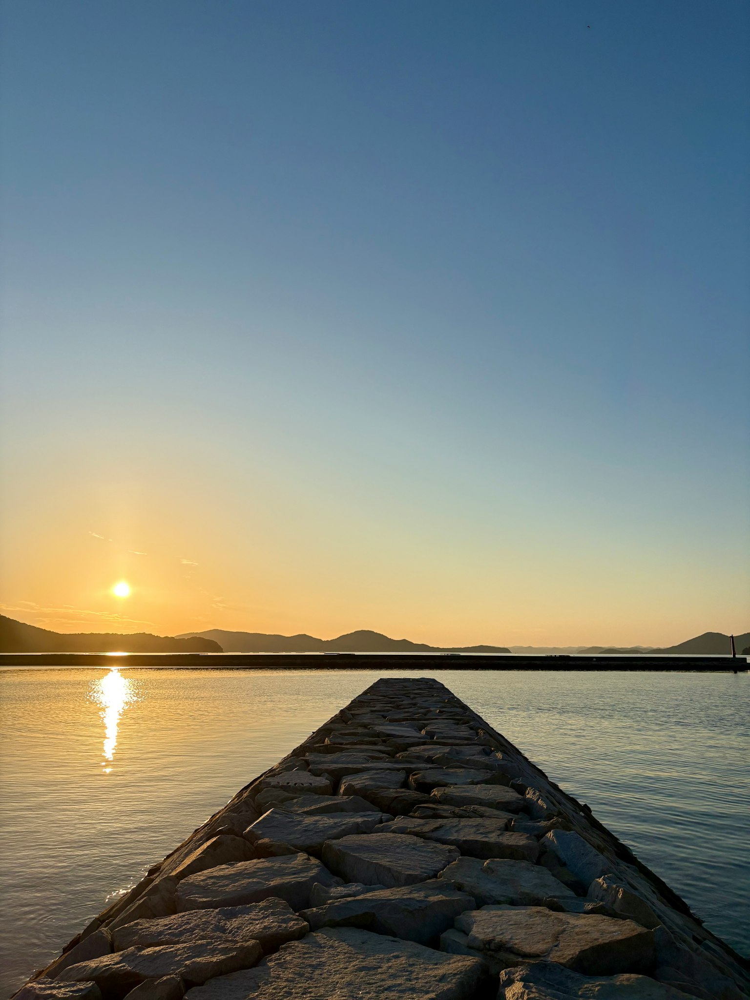 Quai en pierre s'étendant dans l'eau calme avec reflet du coucher de soleil