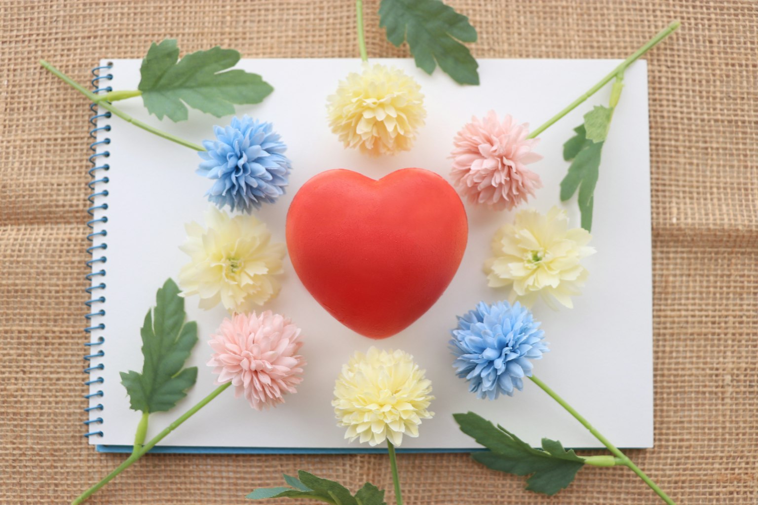 Red heart surrounded by colorful pom-pom flowers on a notebook
