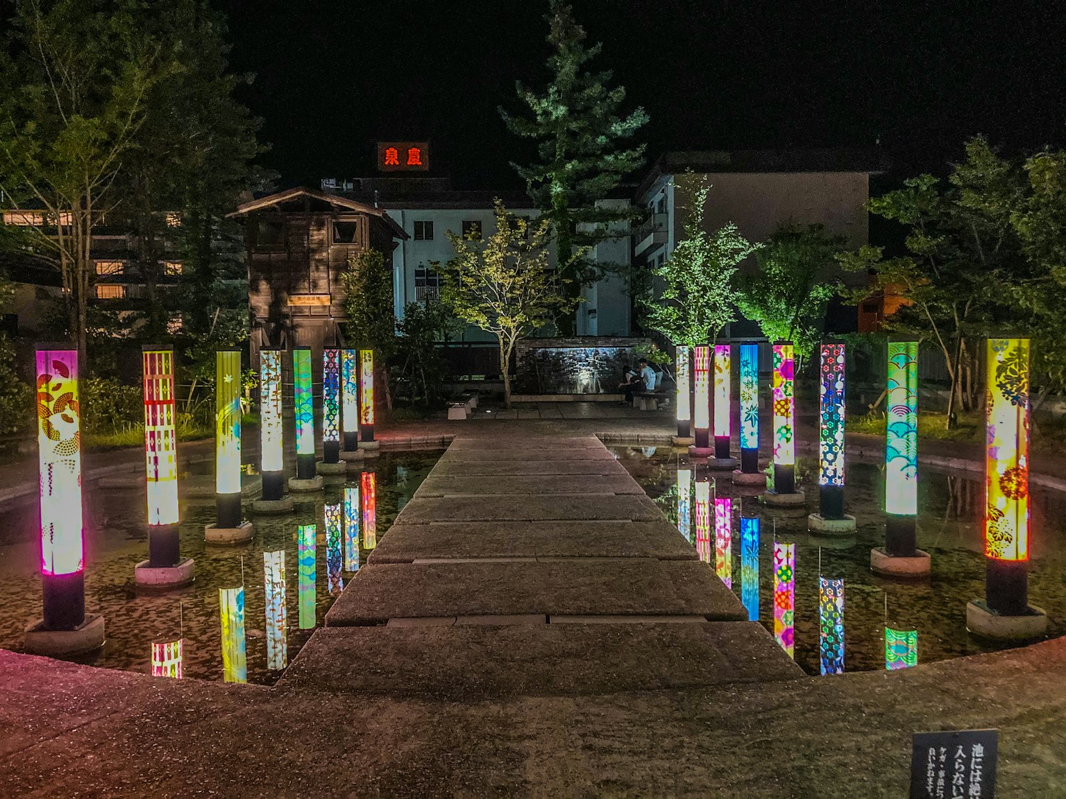 Colonnes illuminées colorées dans un parc nocturne avec des arbres verts