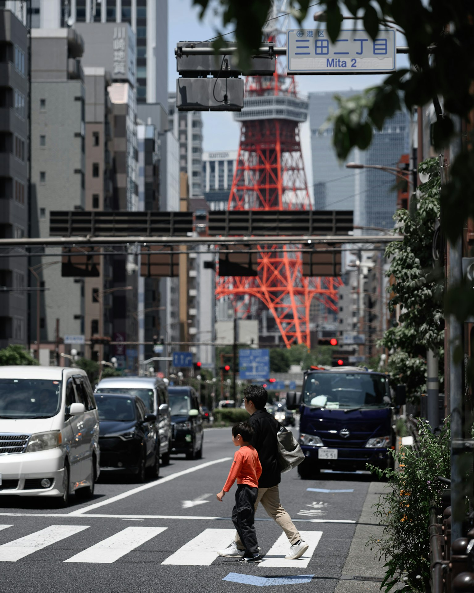 Seorang orang tua dan anak menyeberang jalan dengan Menara Tokyo di latar belakang