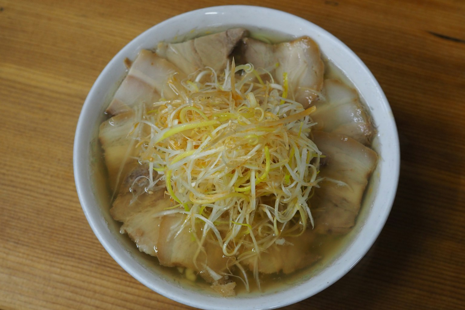 Semangkuk ramen dengan irisan daging babi dan daun bawang cincang dalam kaldu bening