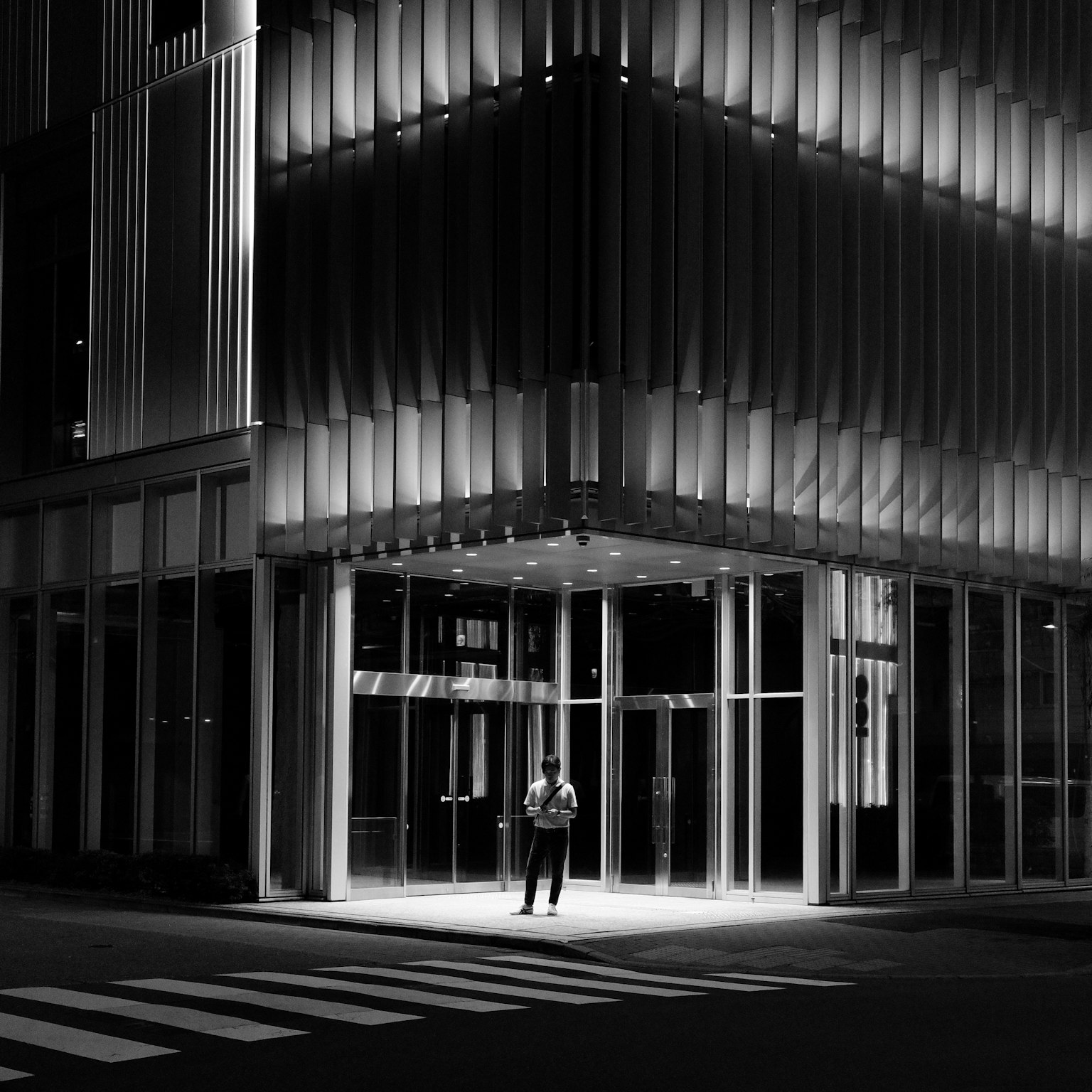 Foto en blanco y negro de una persona de pie frente a un edificio moderno por la noche