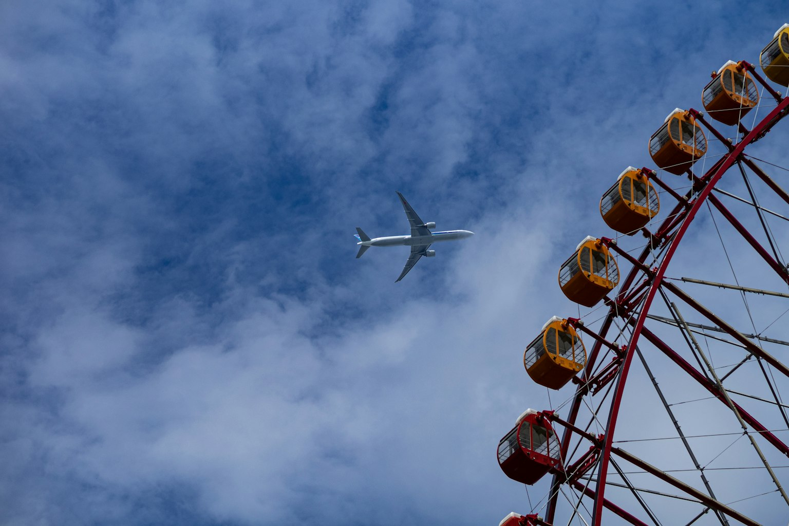 Una scena con una ruota panoramica e un aereo che vola sotto un cielo blu