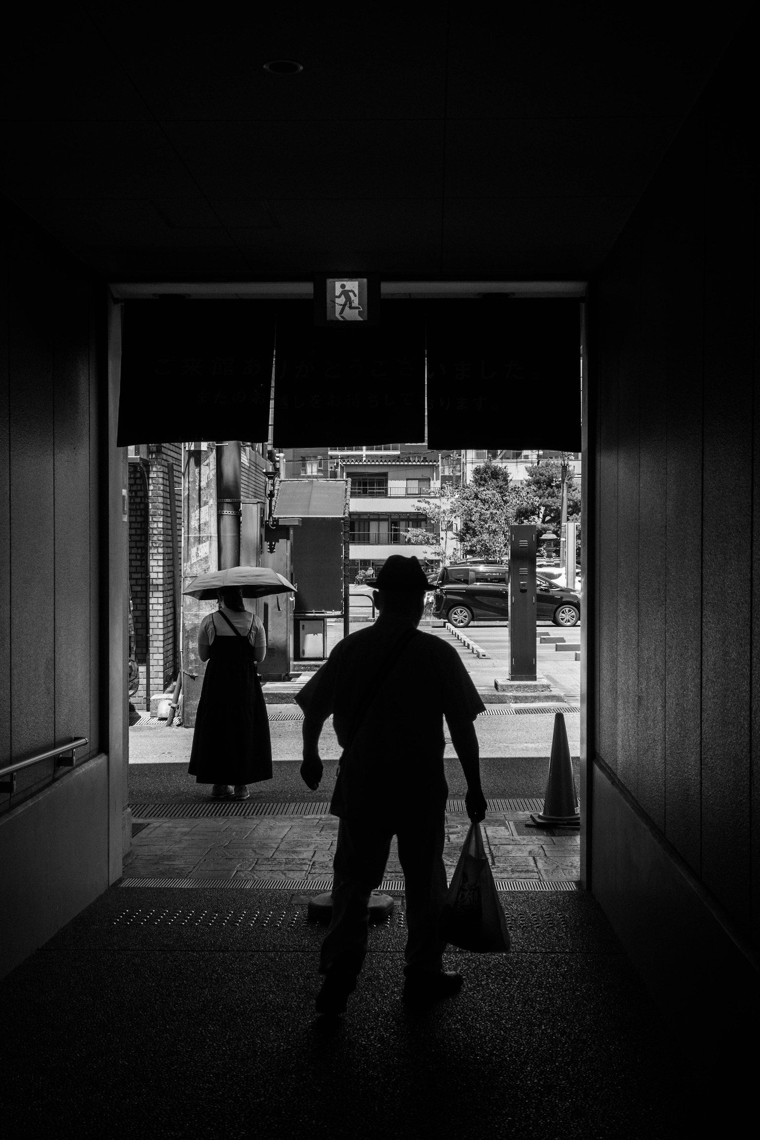 Silhouette d'un homme sortant d'un tunnel sombre avec une femme tenant un parapluie en arrière-plan