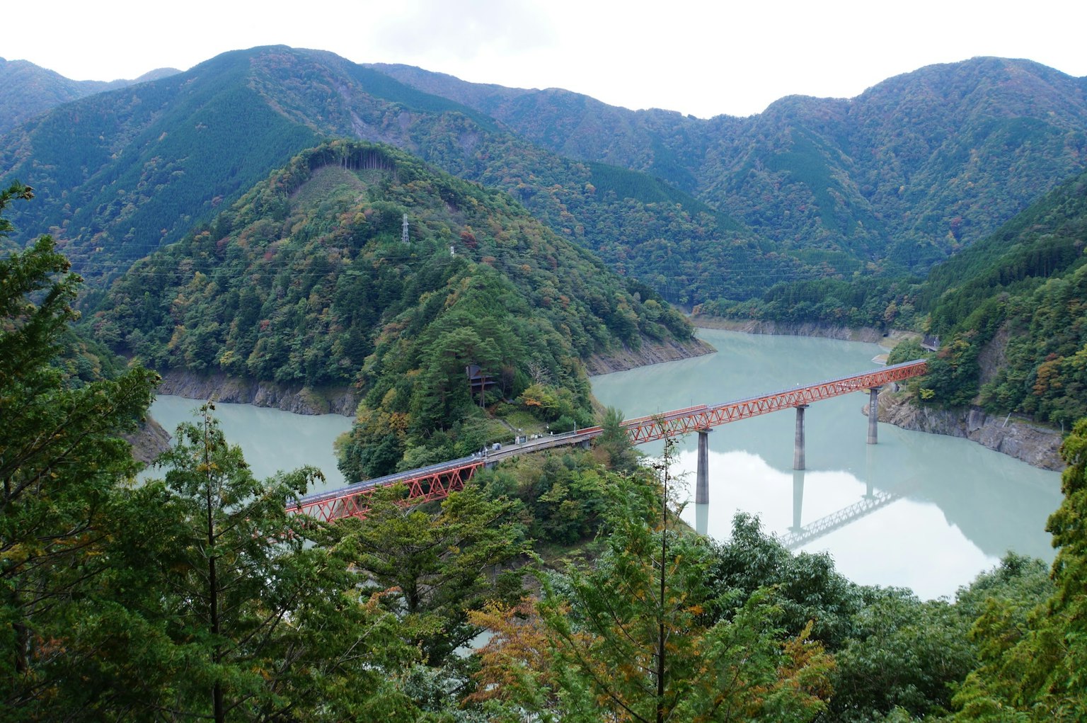 Scenic view of a red bridge spanning a river surrounded by lush green mountains