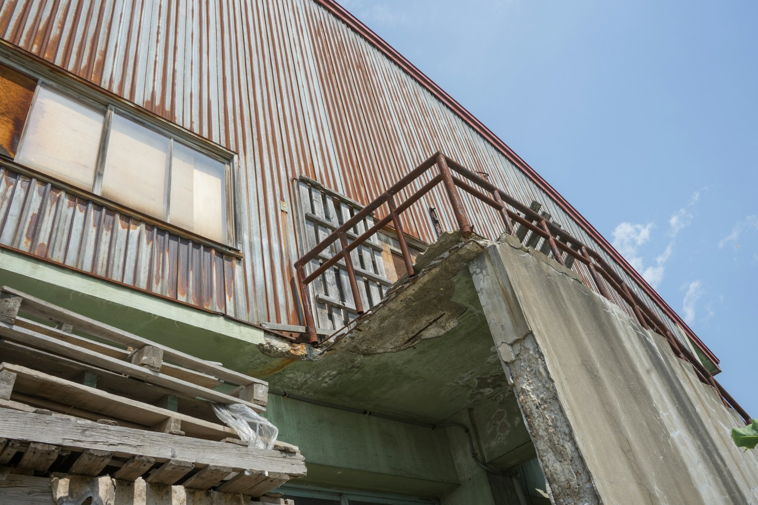 Partie d'un bâtiment avec une façade en métal rouillé et une vieille structure en béton