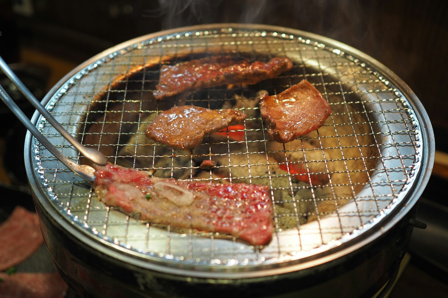 Meat slices grilling on a barbecue with smoke rising