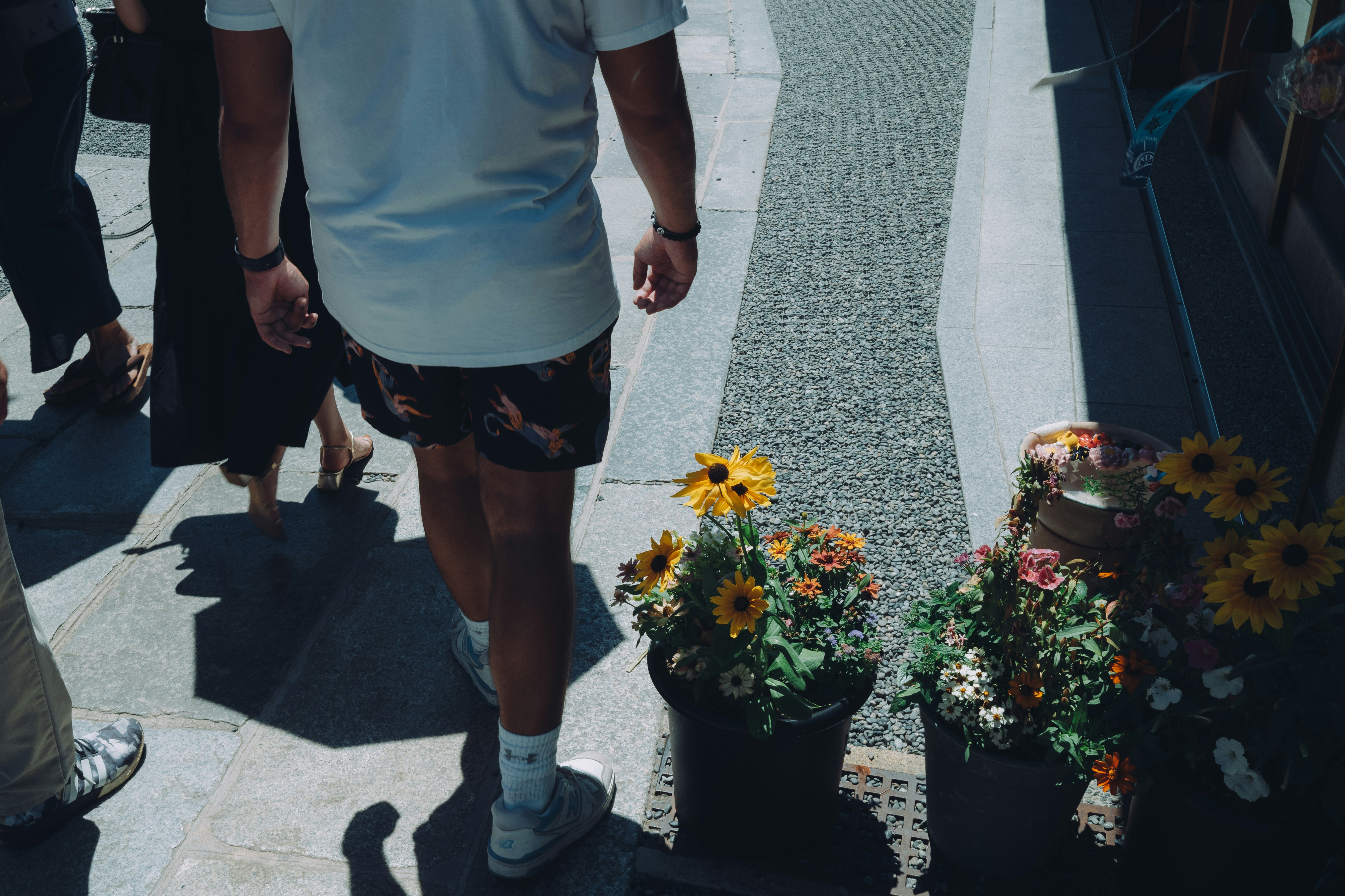 花束とひまわりの鉢植えの前を歩く人々の通路