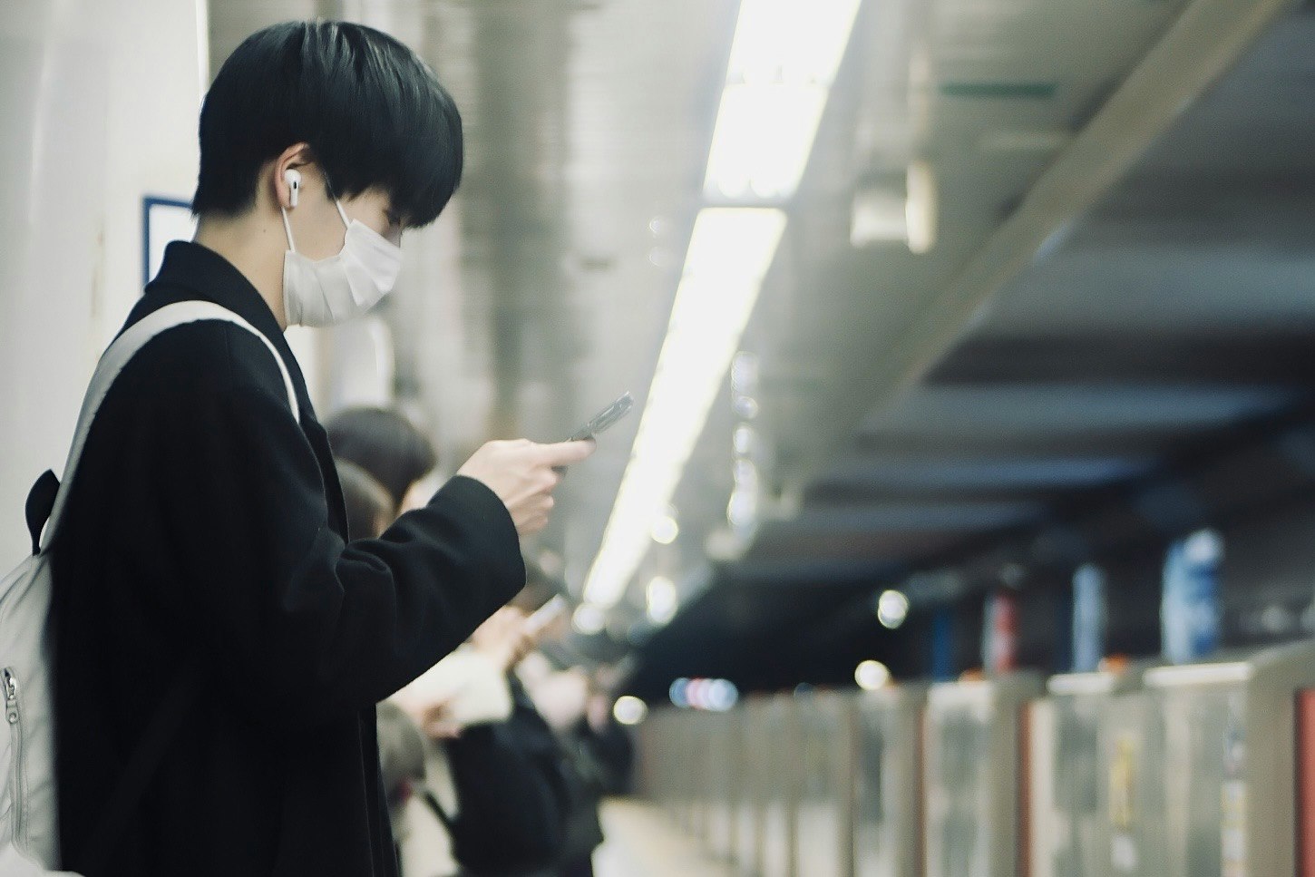 Masked student looking at a smartphone in a hallway