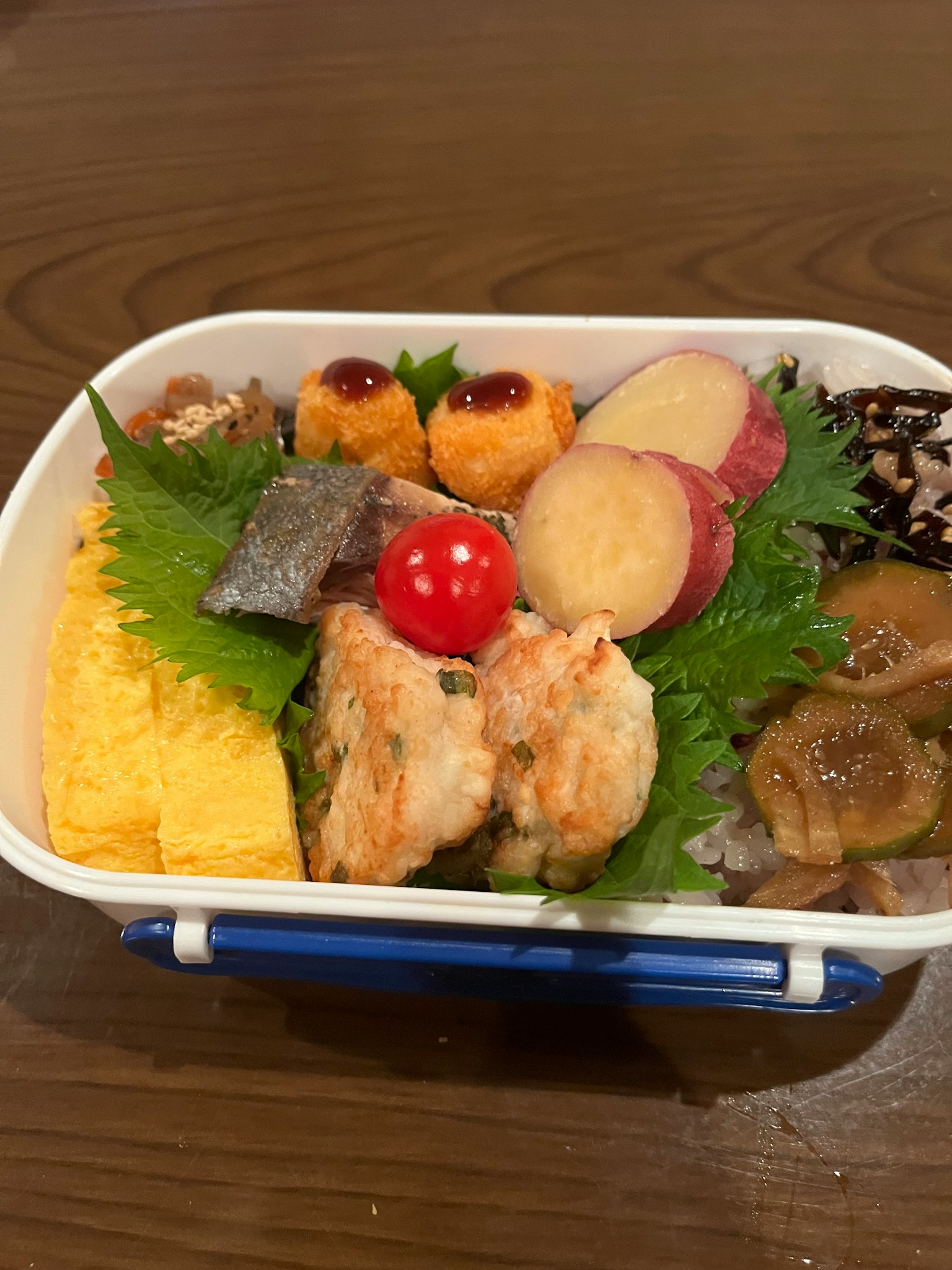 Hộp bento đầy nguyên liệu nhiều màu sắc bao gồm tôm tempura, trứng cuộn, khoai lang và rau củ