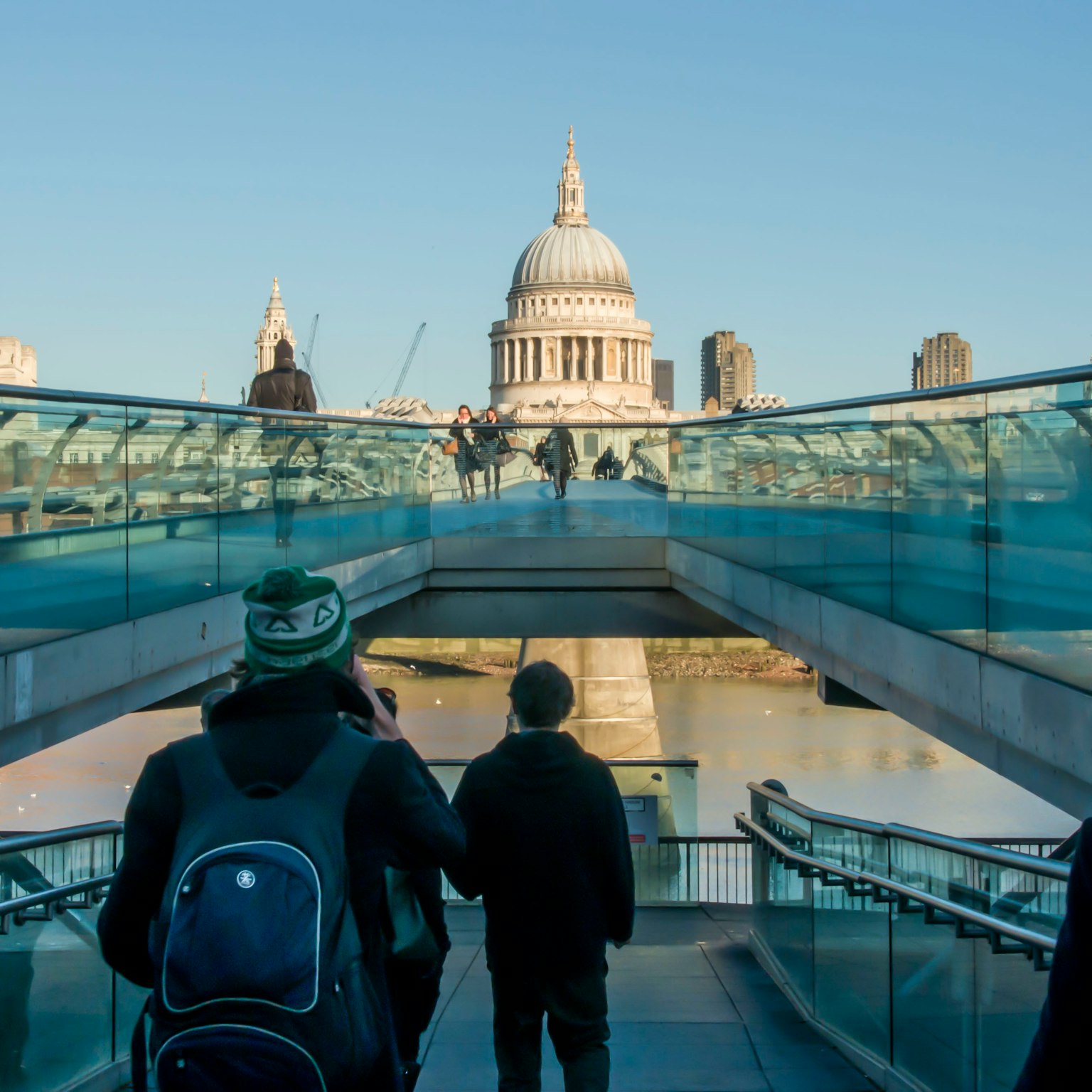 Personas caminando sobre un puente de vidrio con vista a la catedral de San Pablo
