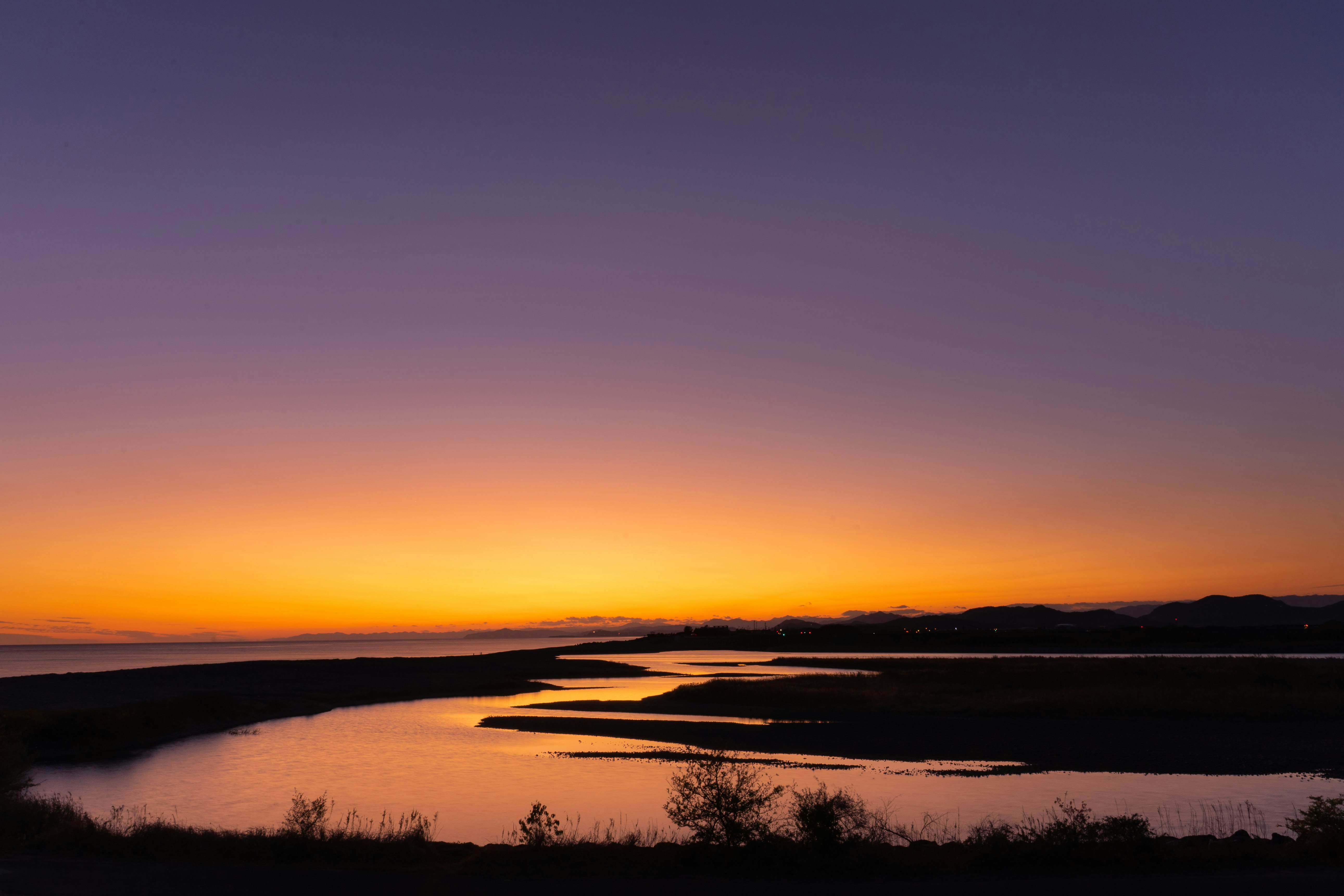 夕焼けの空と川沿いの水面に広がる砂州の風景