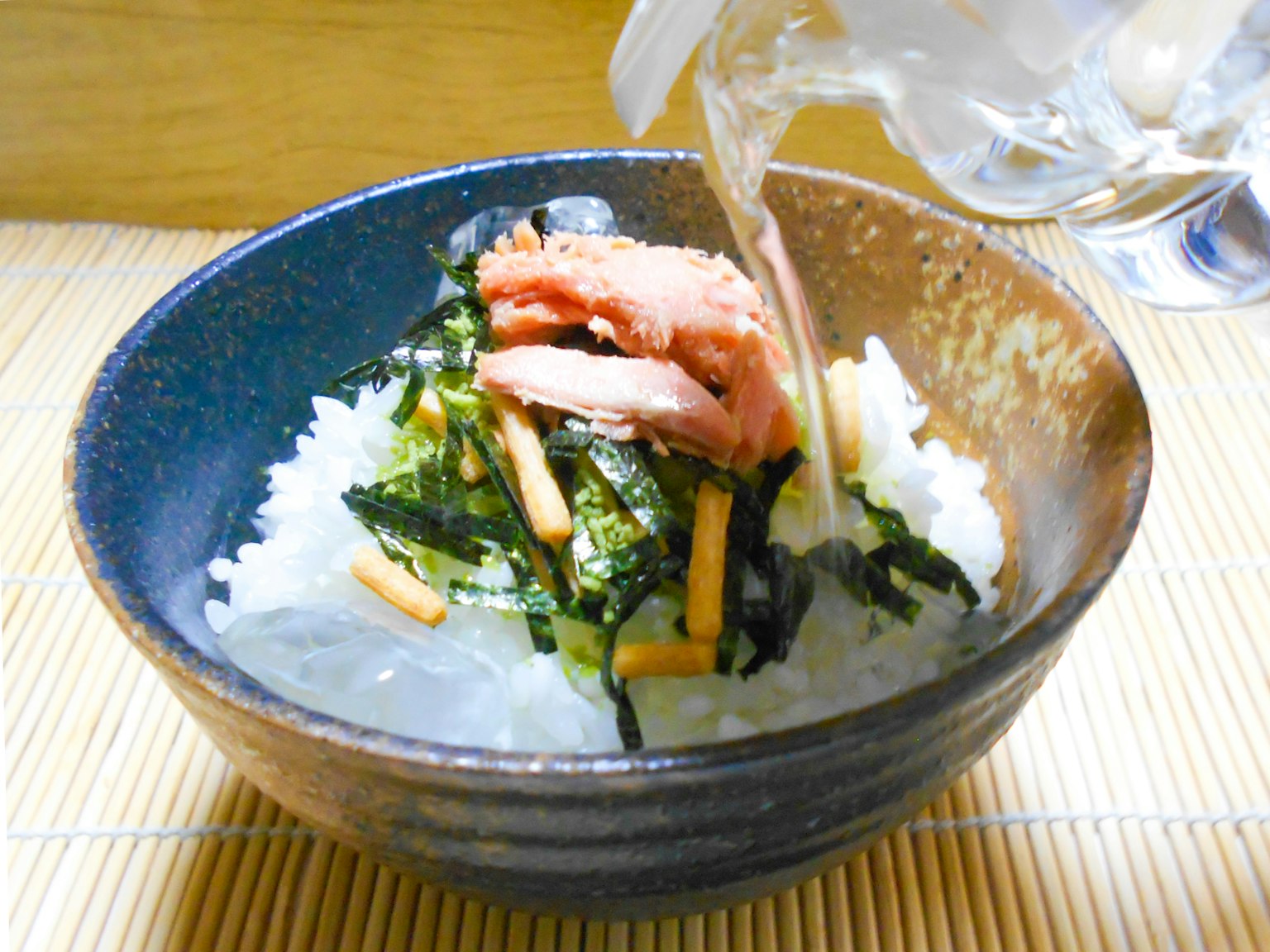 一碗米飯，上面放著海藻和三文魚，正在倒入液體