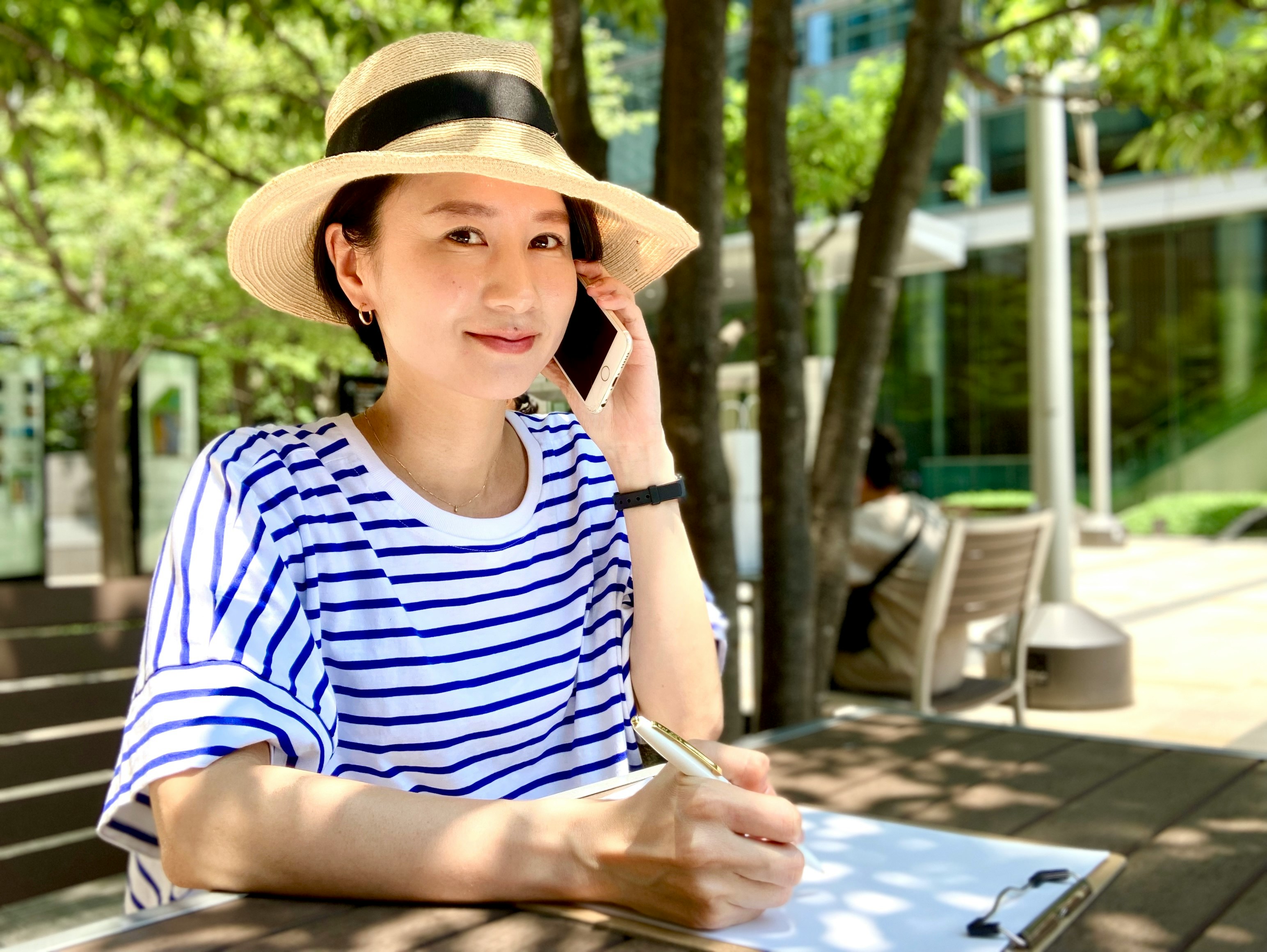树木旁的户外咖啡馆里拿着手机的女性
