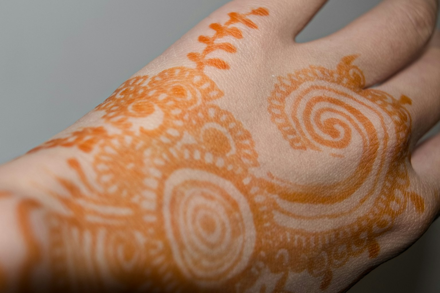 Intricate orange henna design on the hand