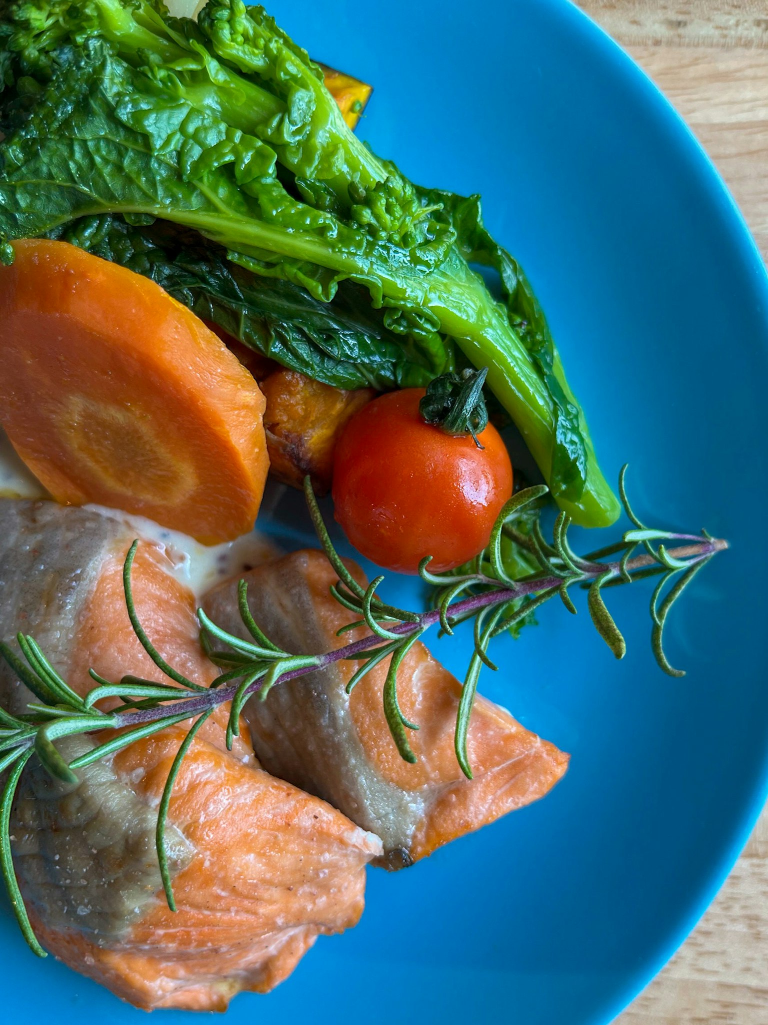 Plat de saumon et légumes sur une assiette bleue comprend une carotte et une tomate cerise garnies de romarin