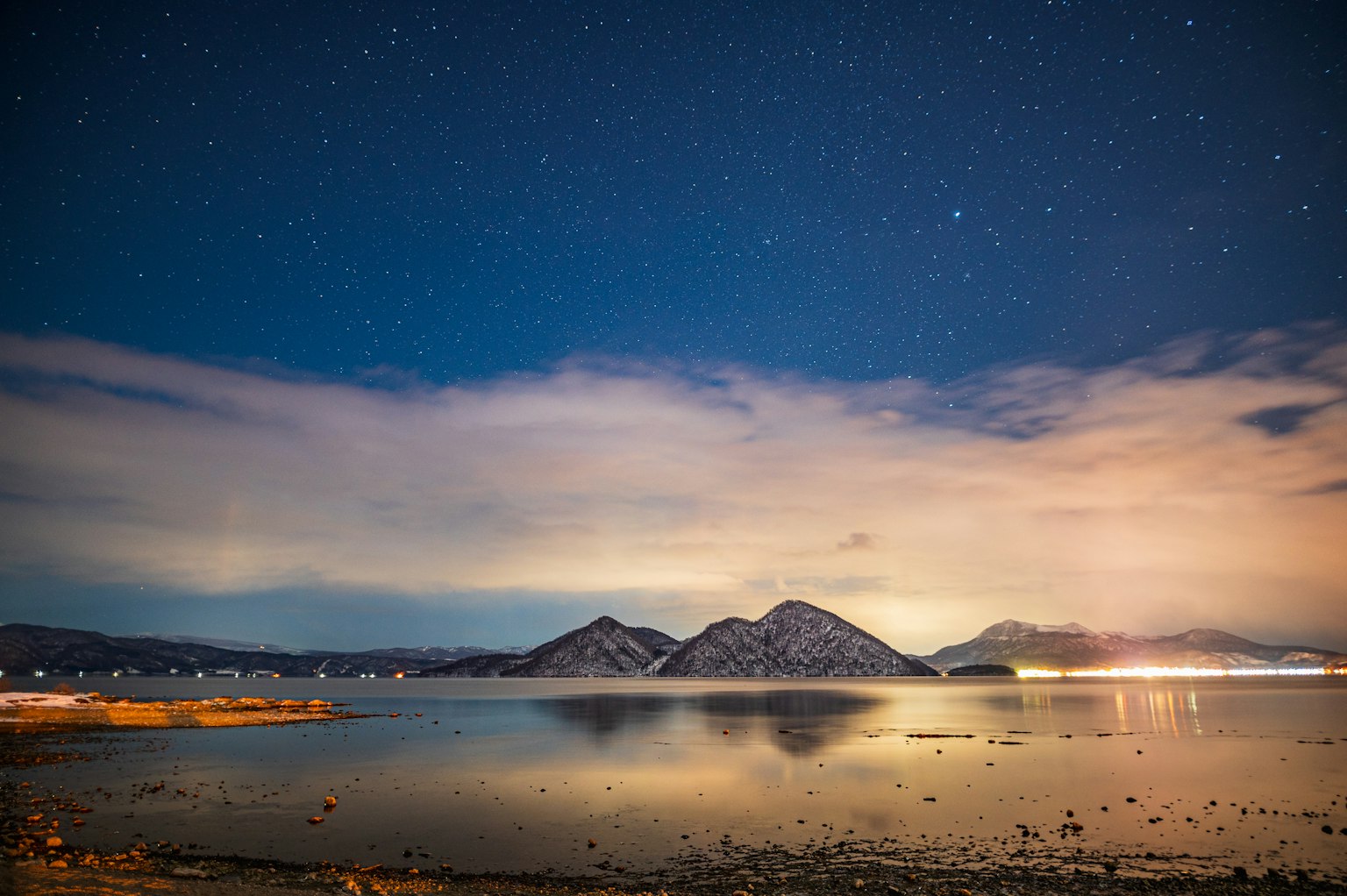 Cielo notturno stellato sopra un lago tranquillo con montagne nebbiose sullo sfondo