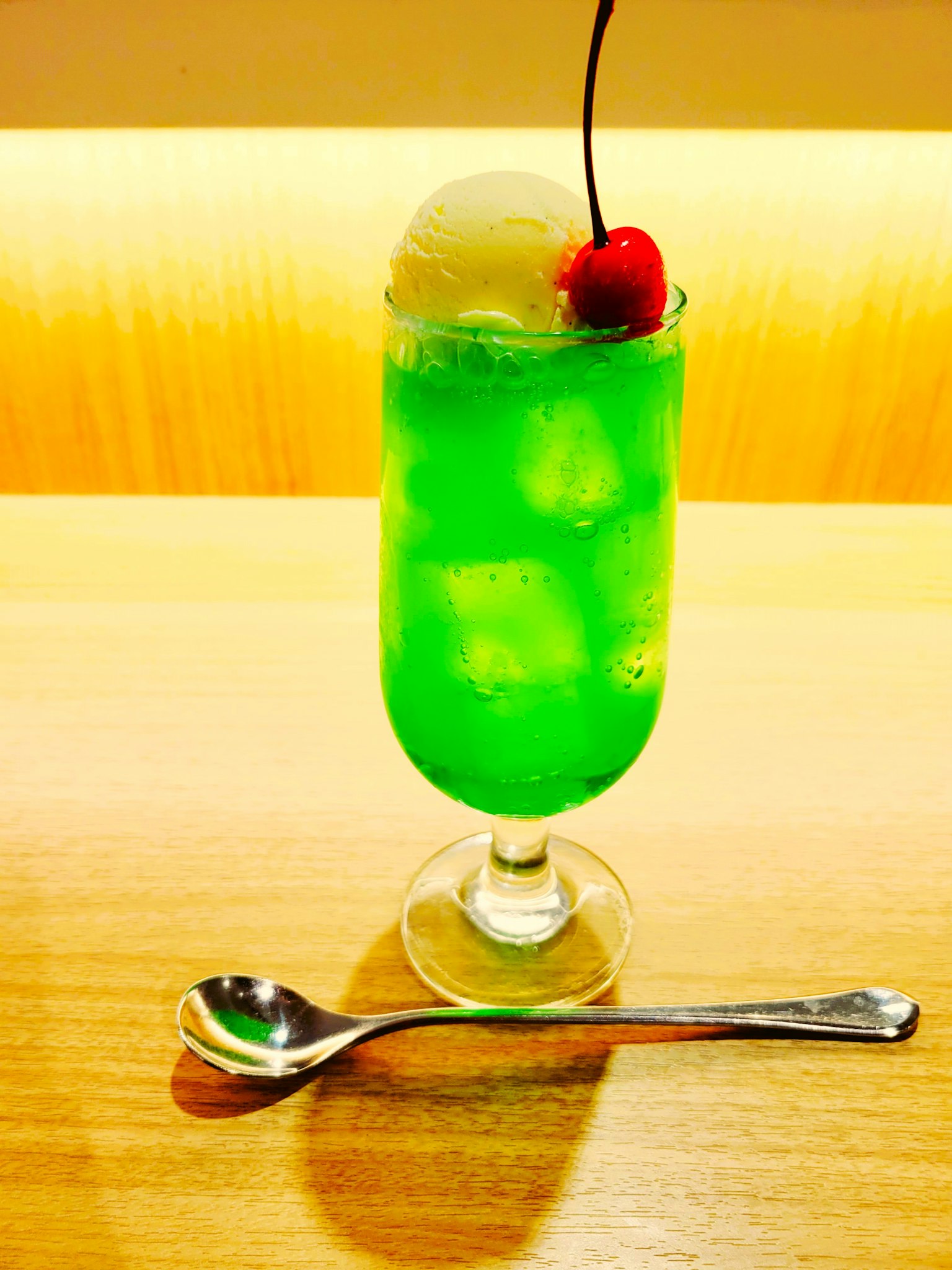 Green beverage topped with vanilla ice cream and cherry in a tall glass