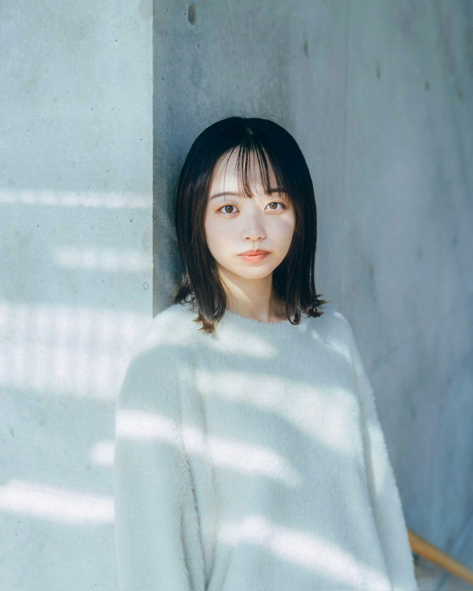 여성이 콘크리트 벽 앞에 서 있고 빛이 그림자를 드리우고 있다