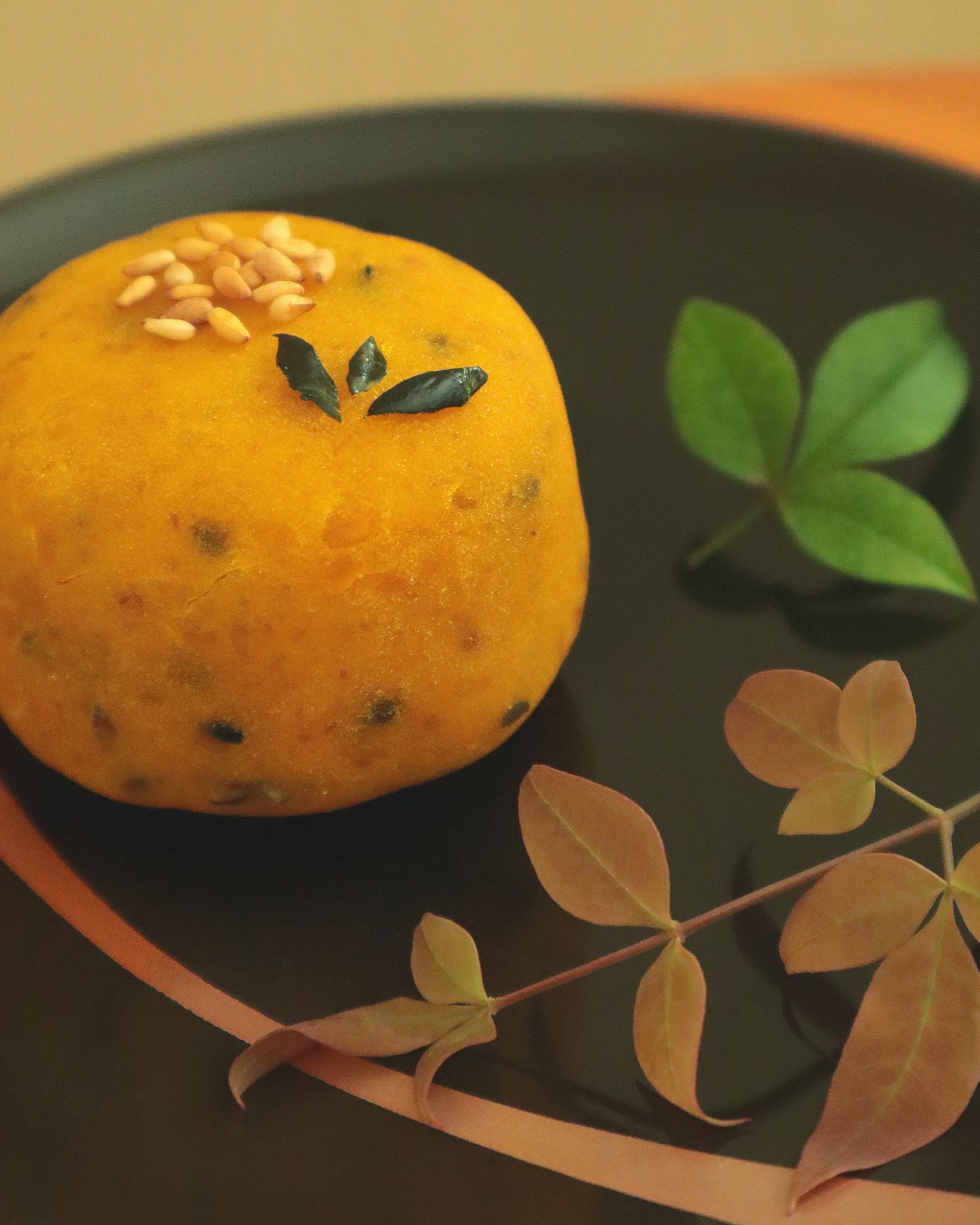 Dessert rotondo arancione su un piatto nero guarnito con semi di sesamo e foglie verdi